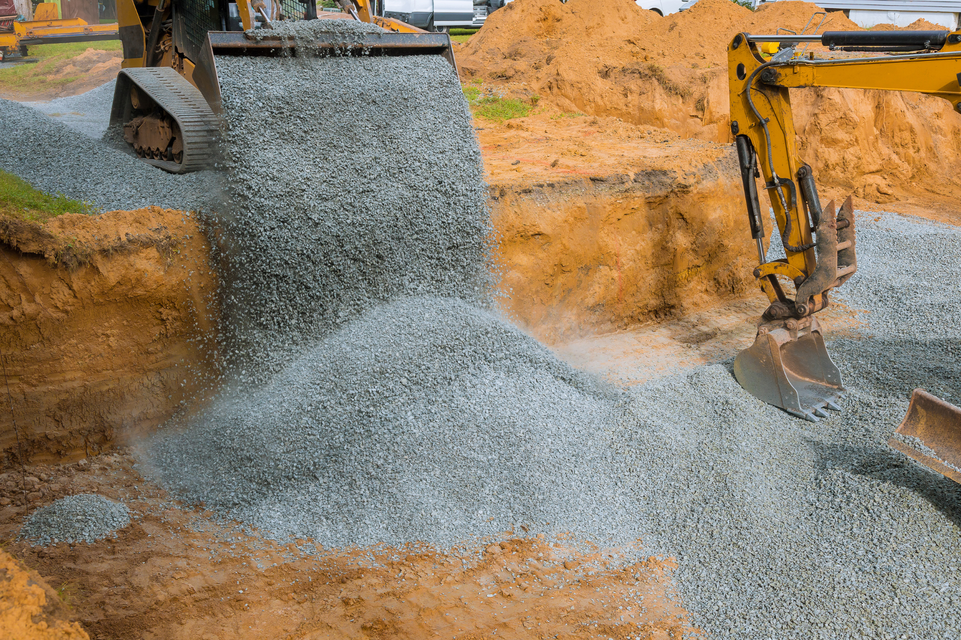 A yellow excavator is loading gravel into a hole.