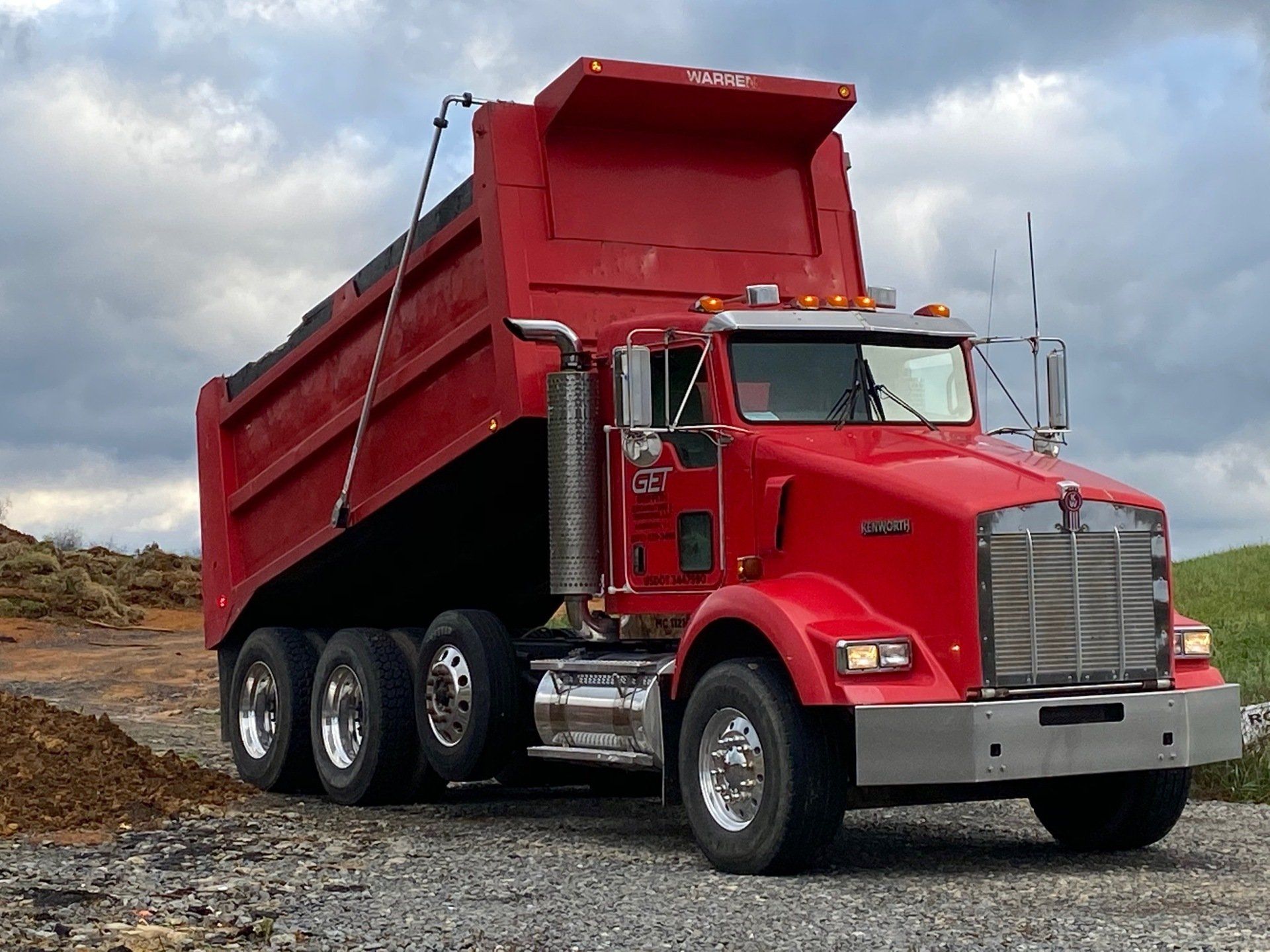 A red dump truck is parked on a gravel road