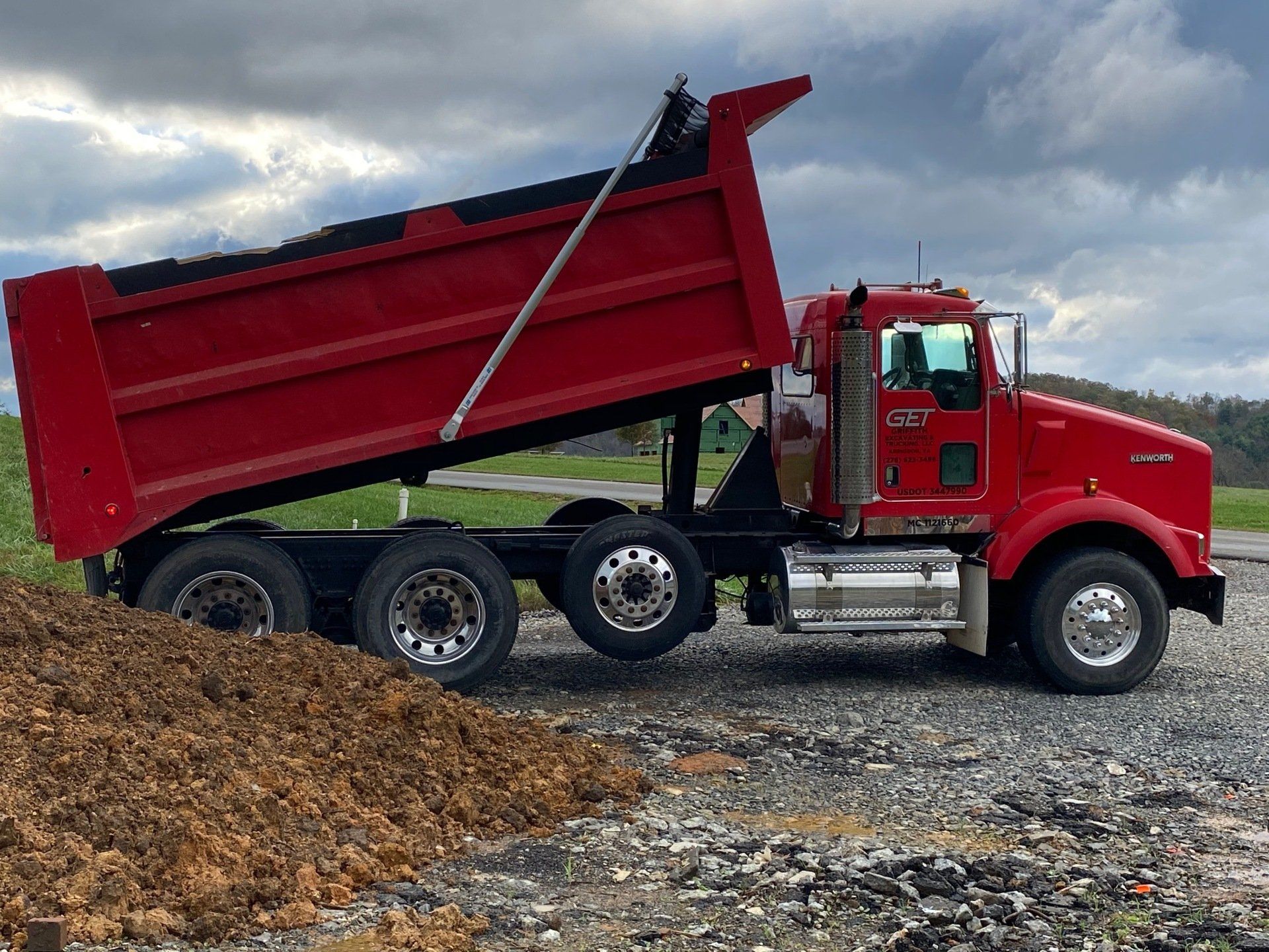 A red dump truck is sitting on a gravel road.