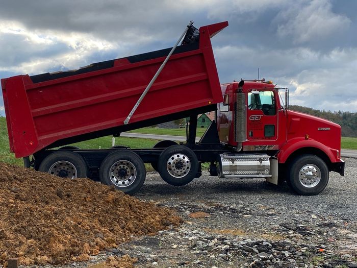 A red dump truck is parked next to a pile of dirt.