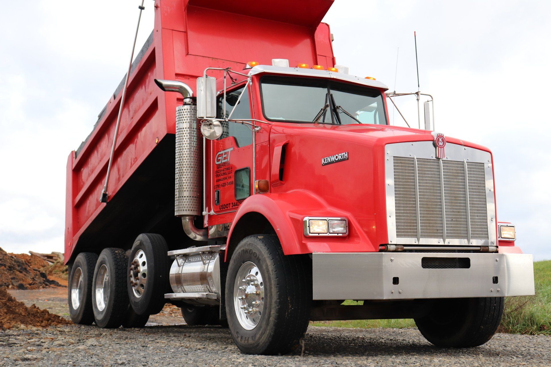 A red dump truck is parked on a gravel road.