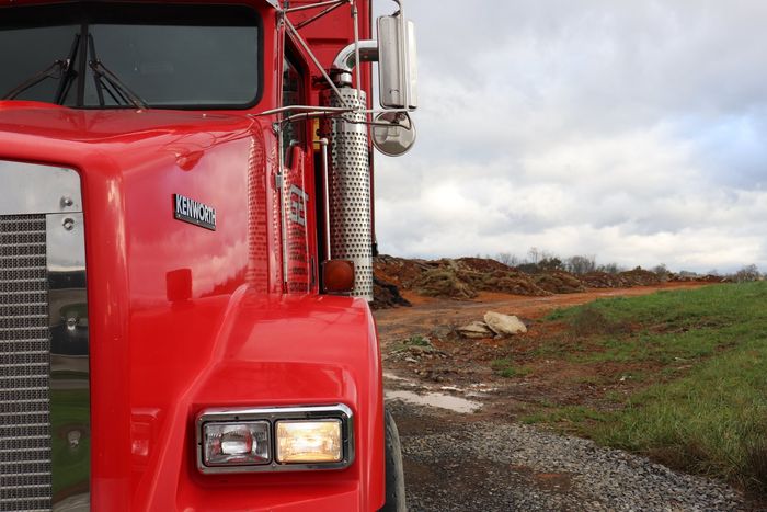 A red semi truck is parked on the side of a dirt road.