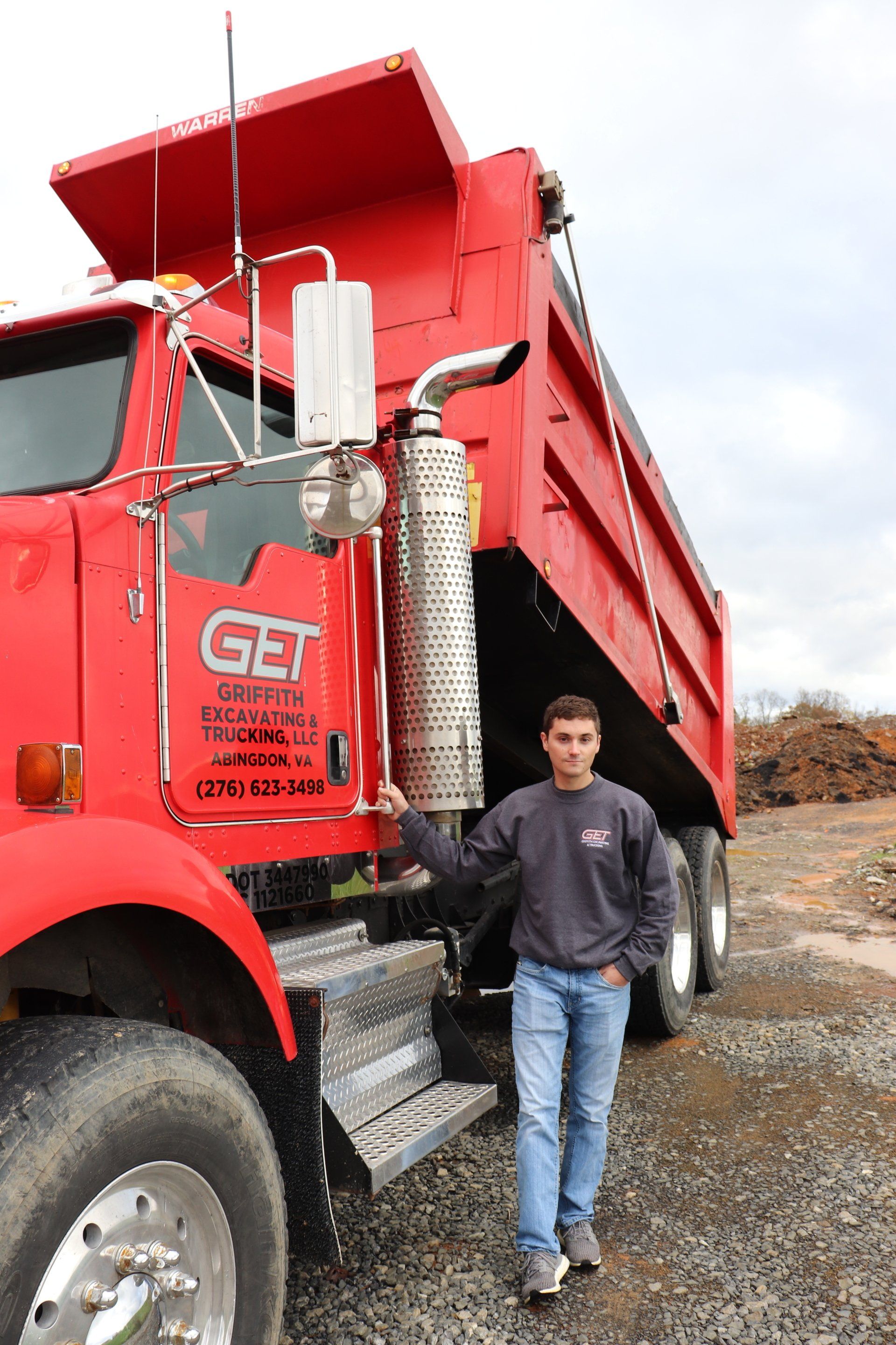 A young man is standing in front of a red dump truck.
