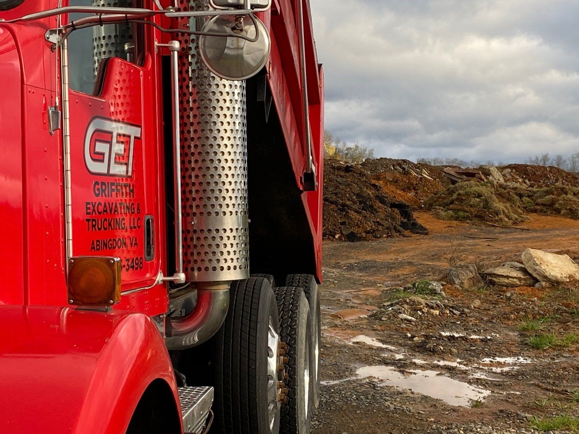 A red dump truck is parked in a dirt field.