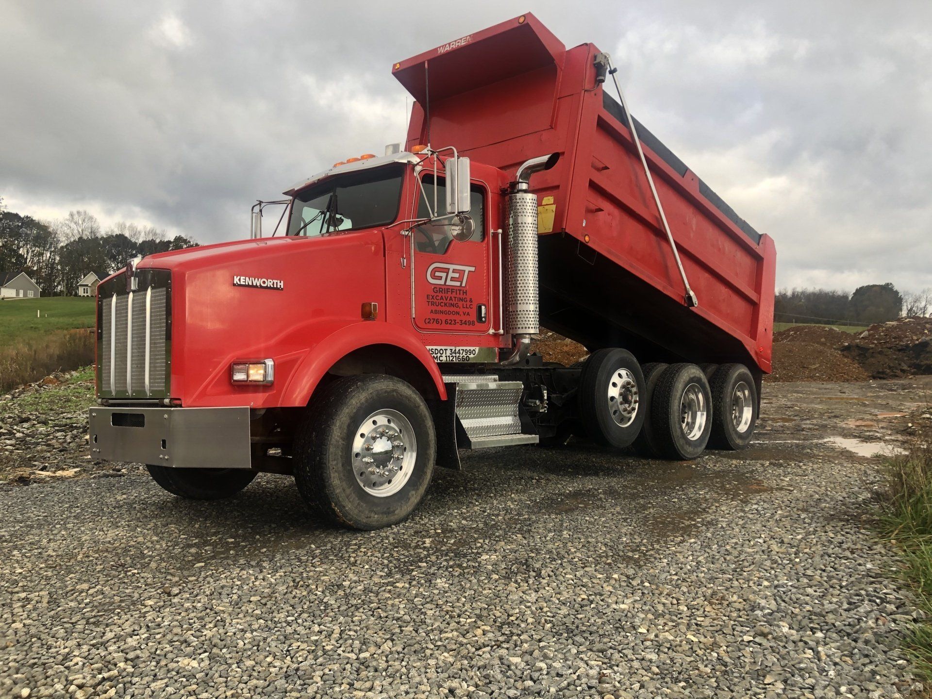 A red dump truck is parked on a gravel road.