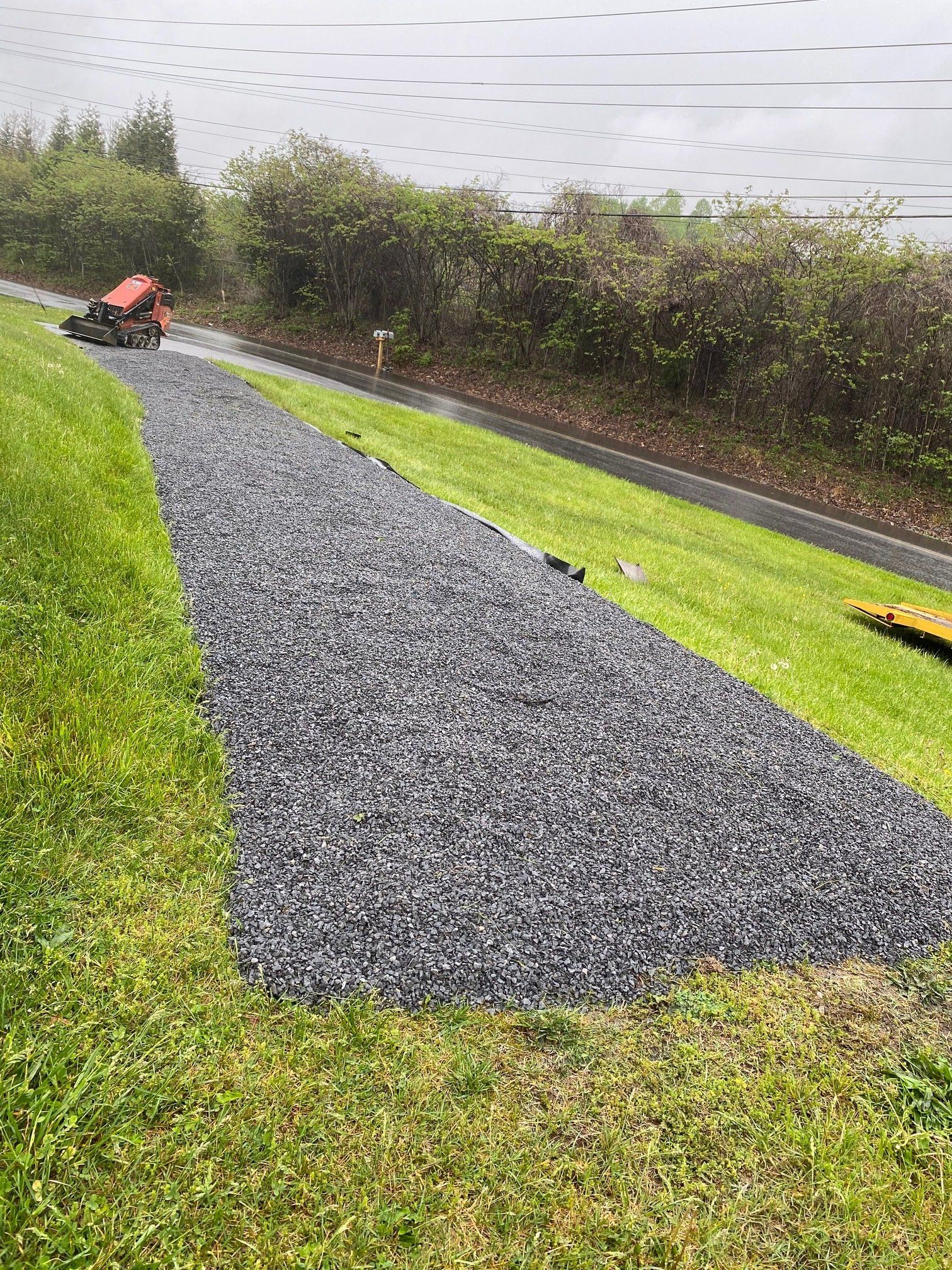 A lawn mower is cutting grass on the side of a road next to a body of water.