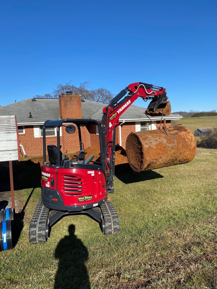 A red excavator is loading a large log into a bucket in front of a house.