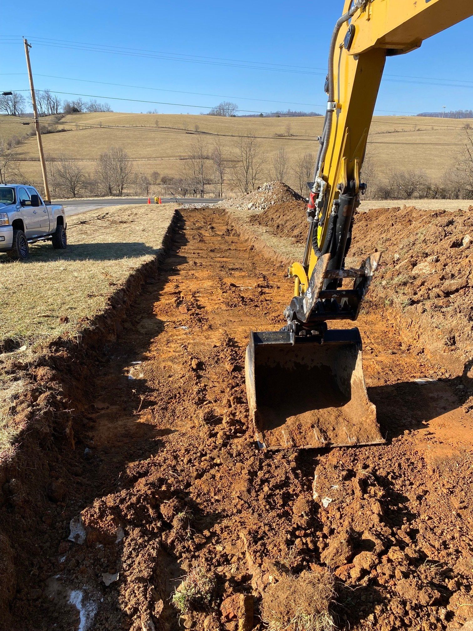 A yellow excavator is digging a hole in the dirt next to a truck.