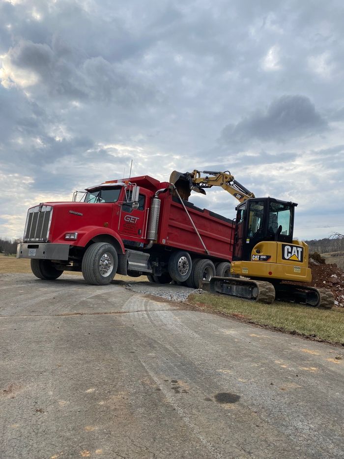 A red dump truck is being loaded with dirt by a yellow excavator.