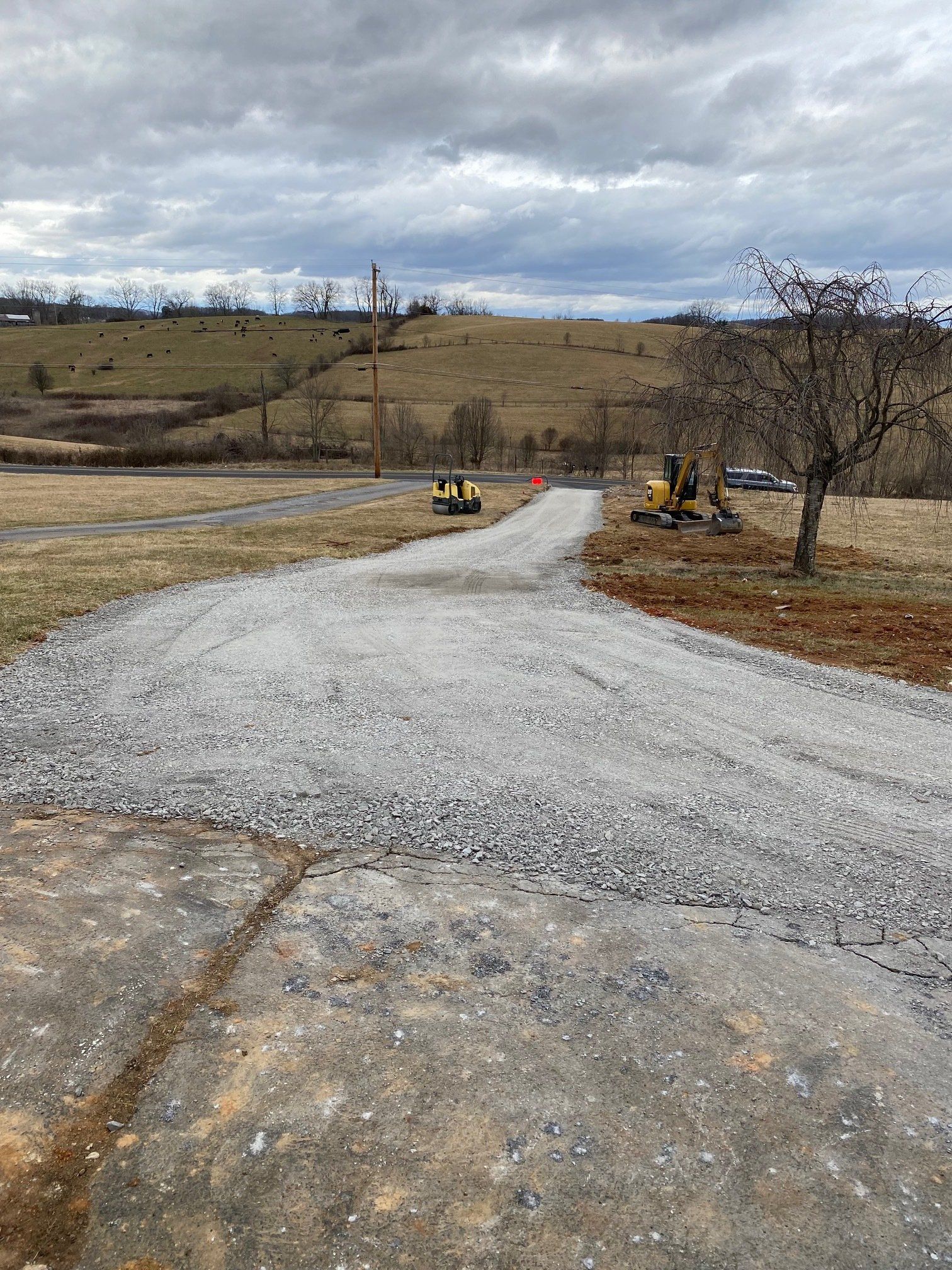 A gravel road with a yellow excavator on the side of it.