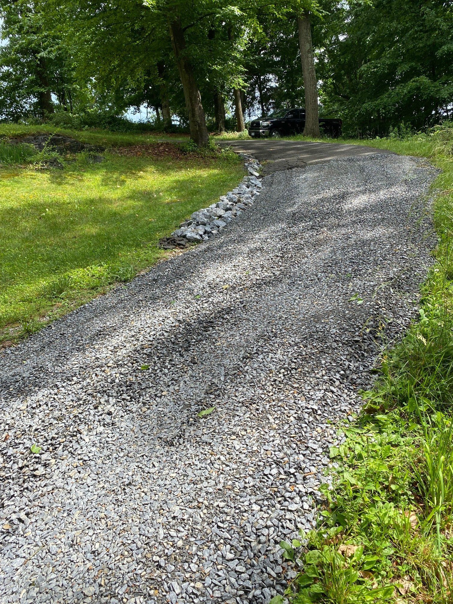 A gravel road going through a grassy field with trees on both sides.