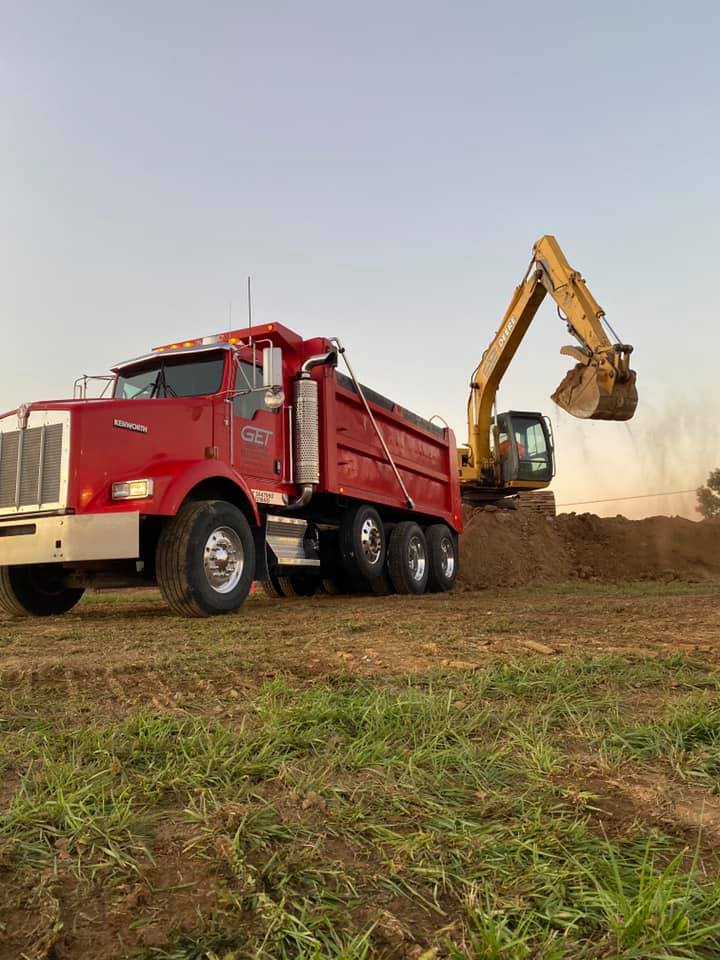 A red dump truck is parked next to a yellow excavator in a field.