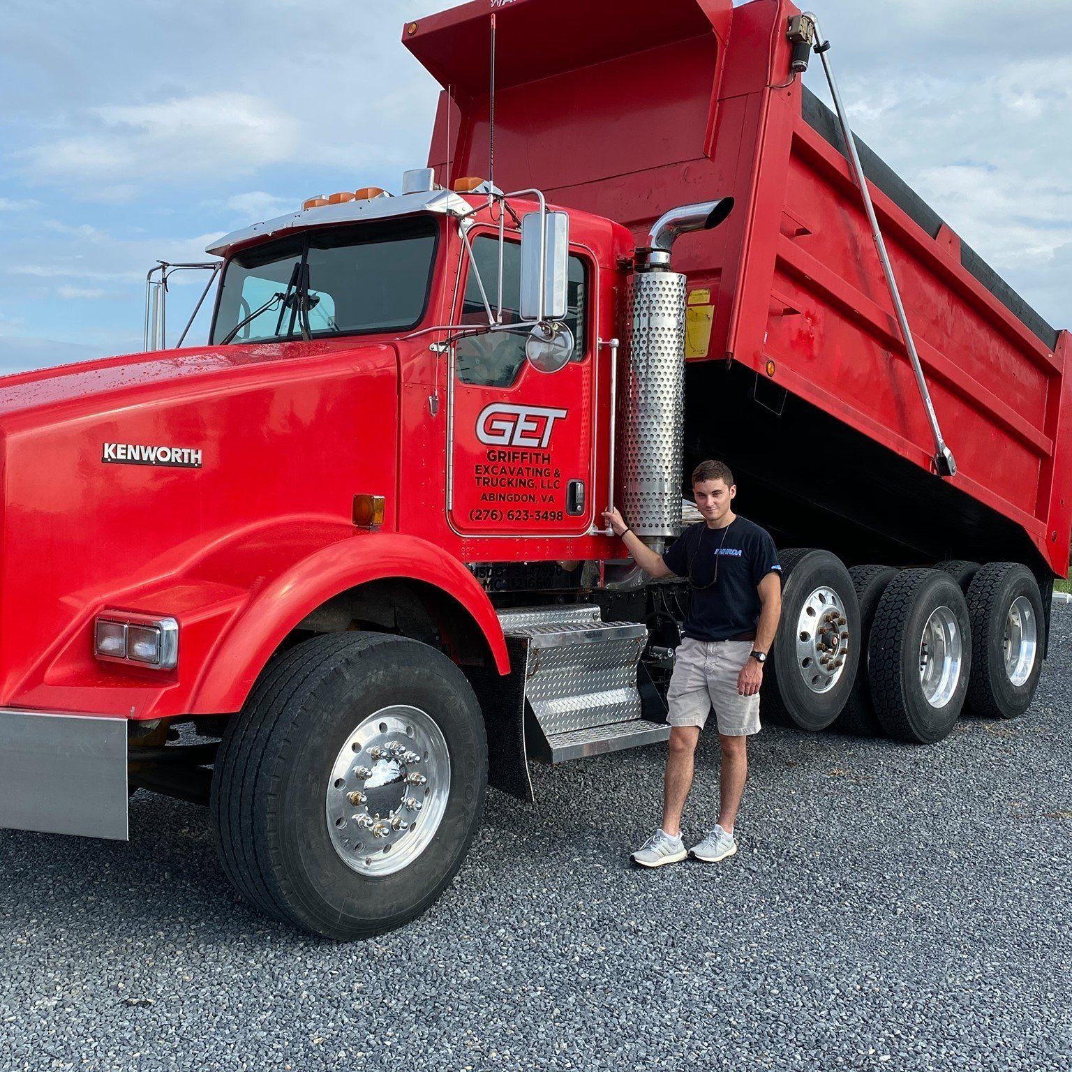 A man is standing in front of a red dump truck.