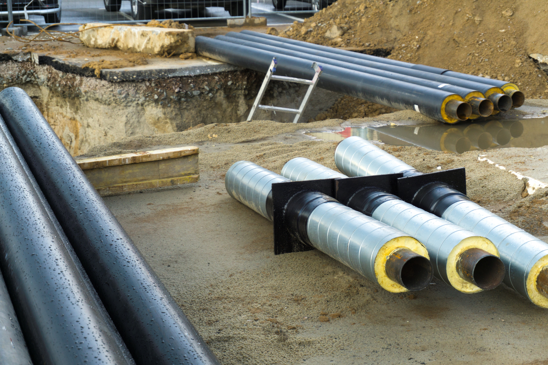 A bunch of pipes are laying in the dirt on a construction site.