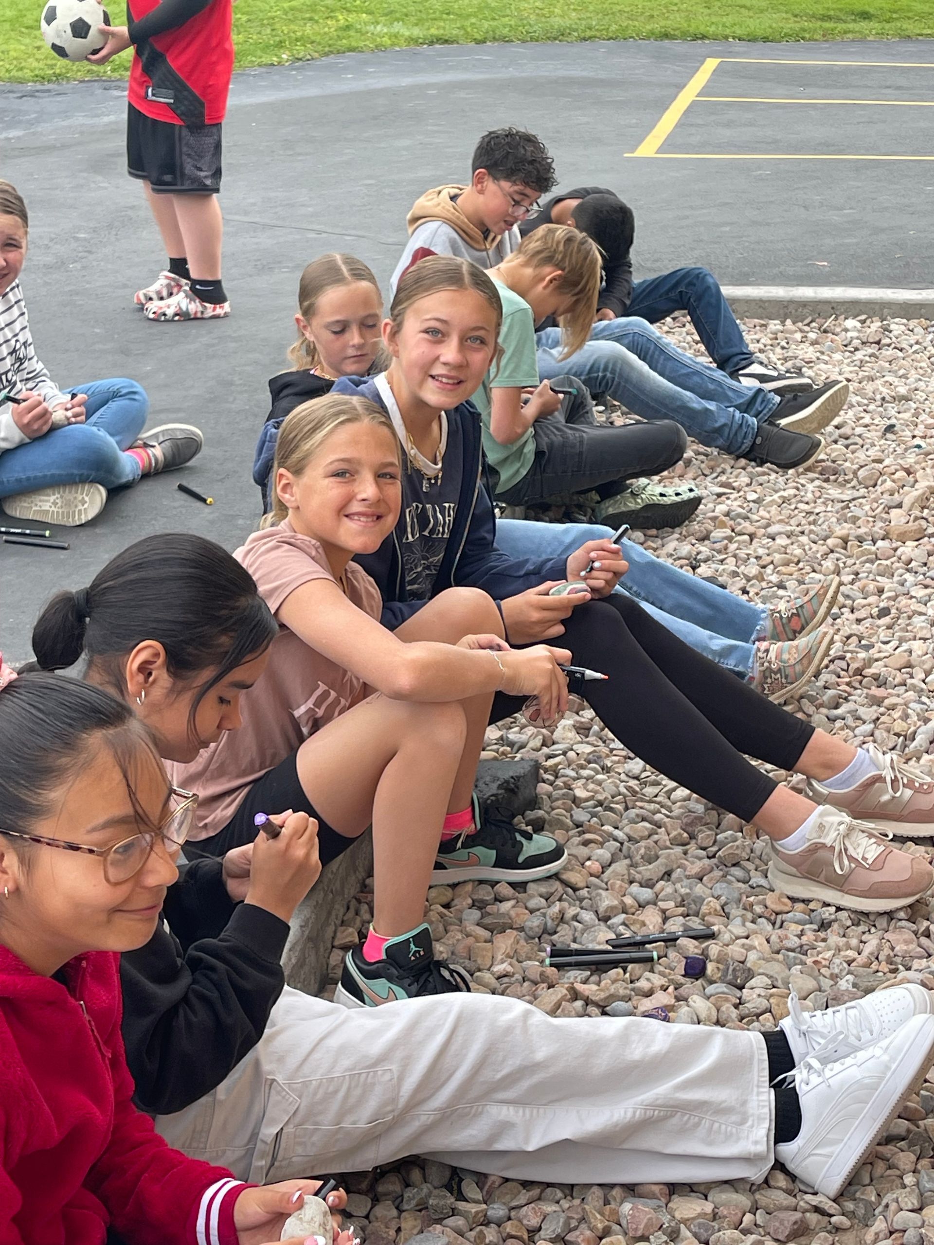Sixth grade students smiling while they paint rocks.