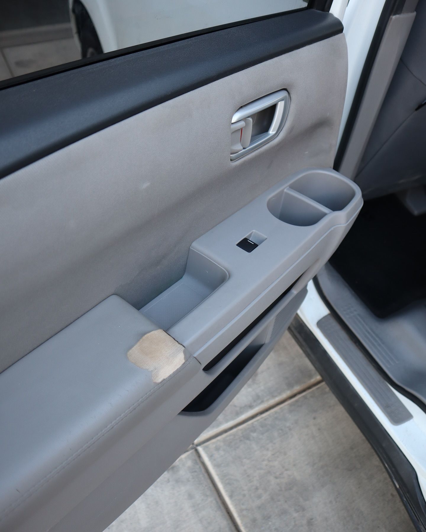 Car door interior; gray panel with worn armrest, handle, and cup holder.