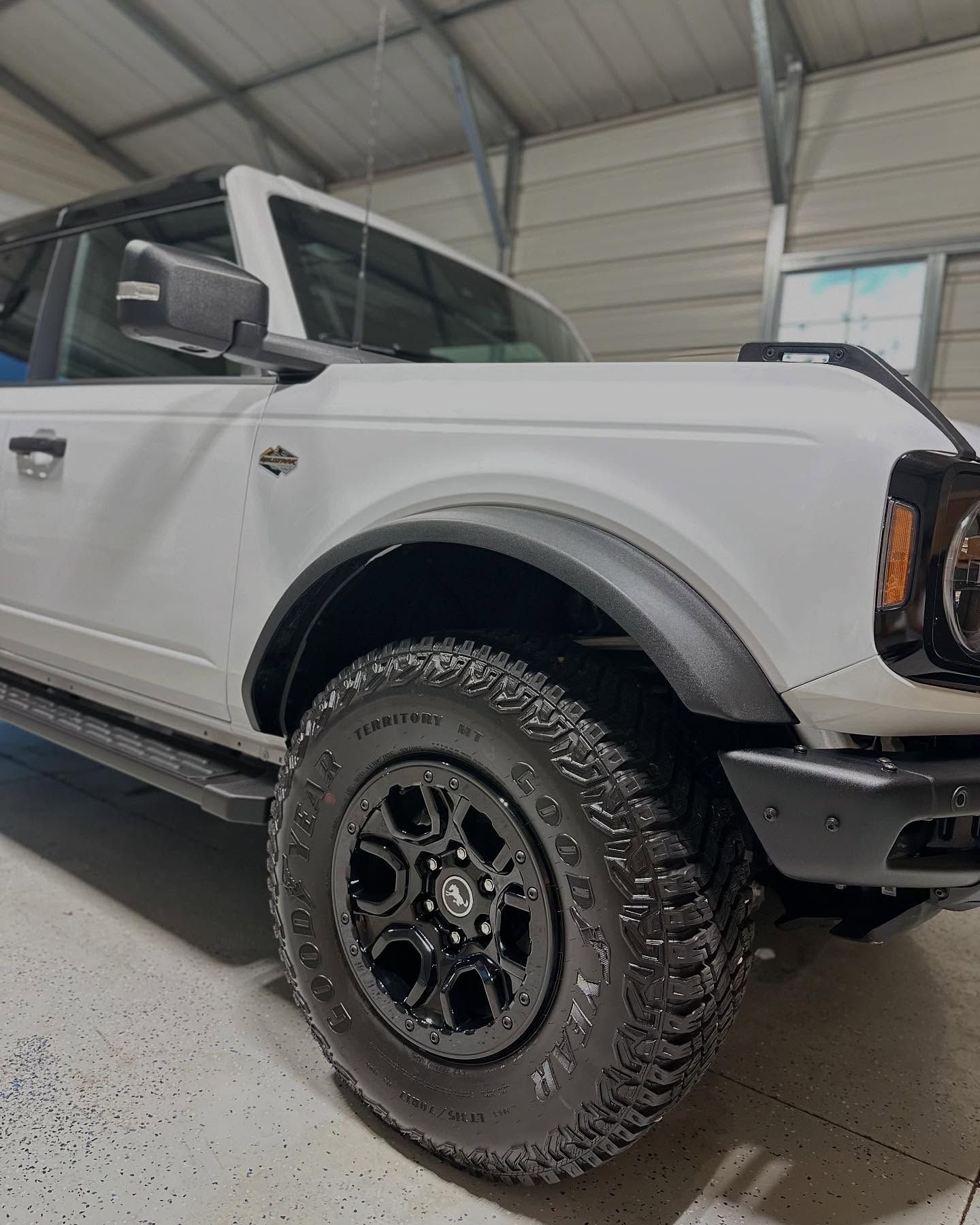 White Ford Bronco with black accents and off-road tires, parked inside a garage.