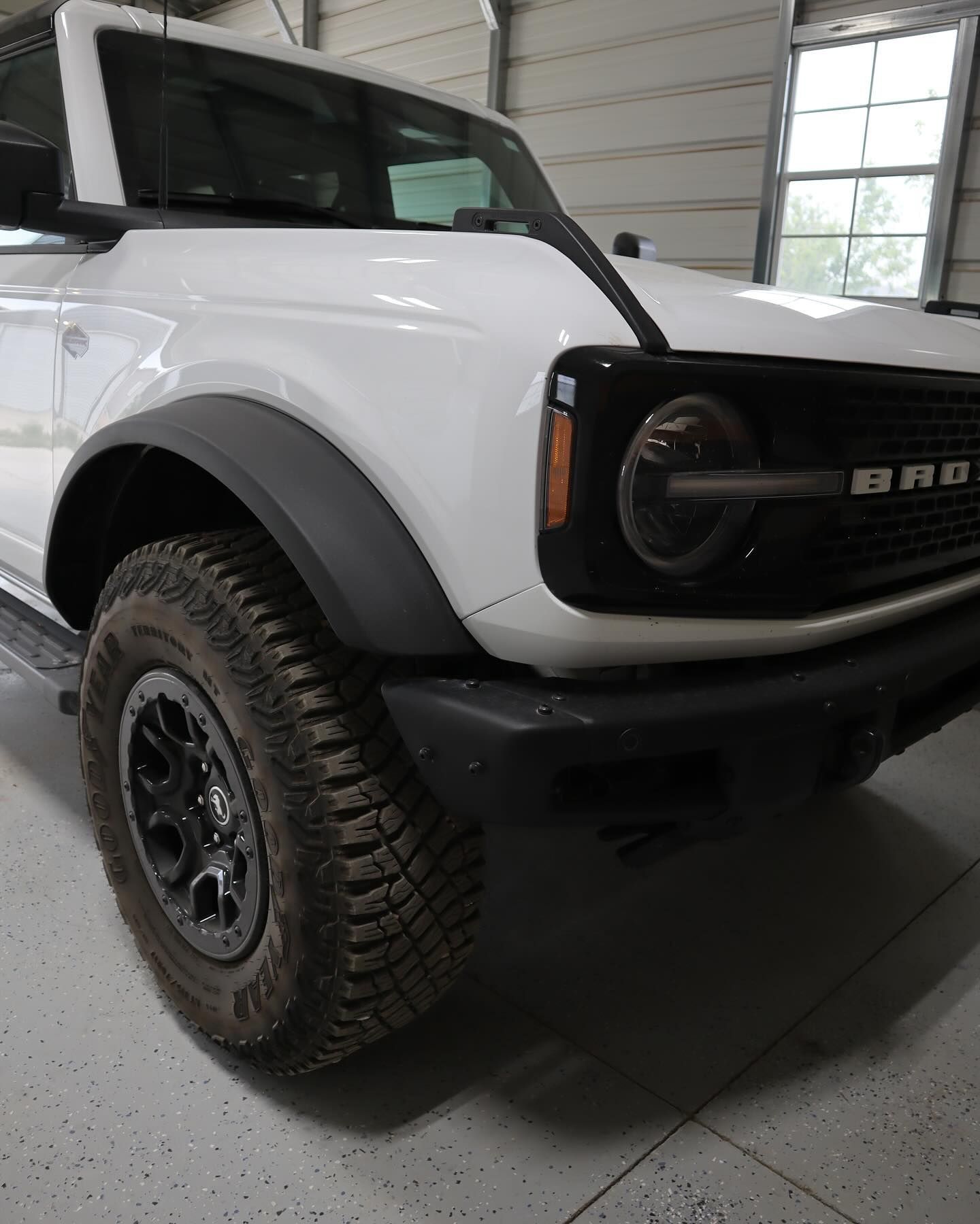 White Ford Bronco, black fender flares and front bumper, inside a garage with a window.
