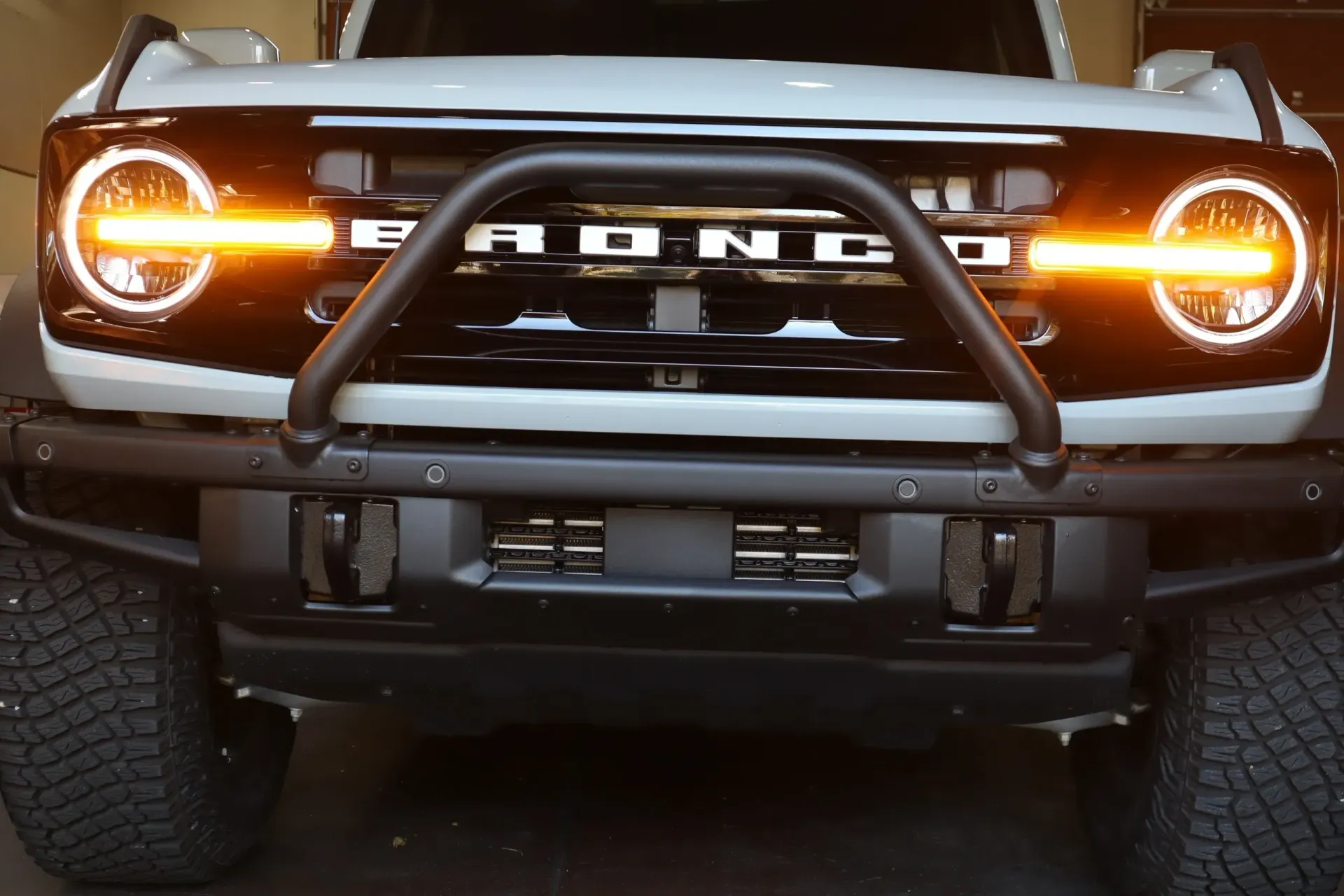 White Ford Bronco with black bumper and bull bar; headlights illuminated.