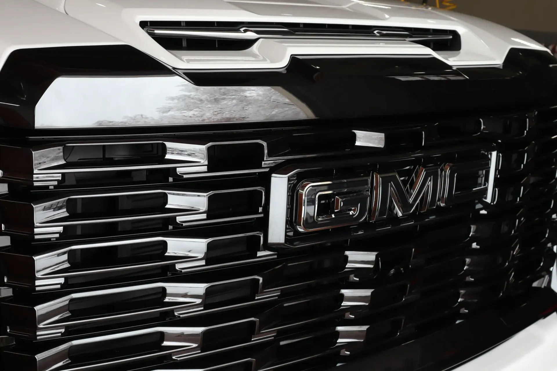 Black and chrome GMC truck grille with white hood and GMC logo.