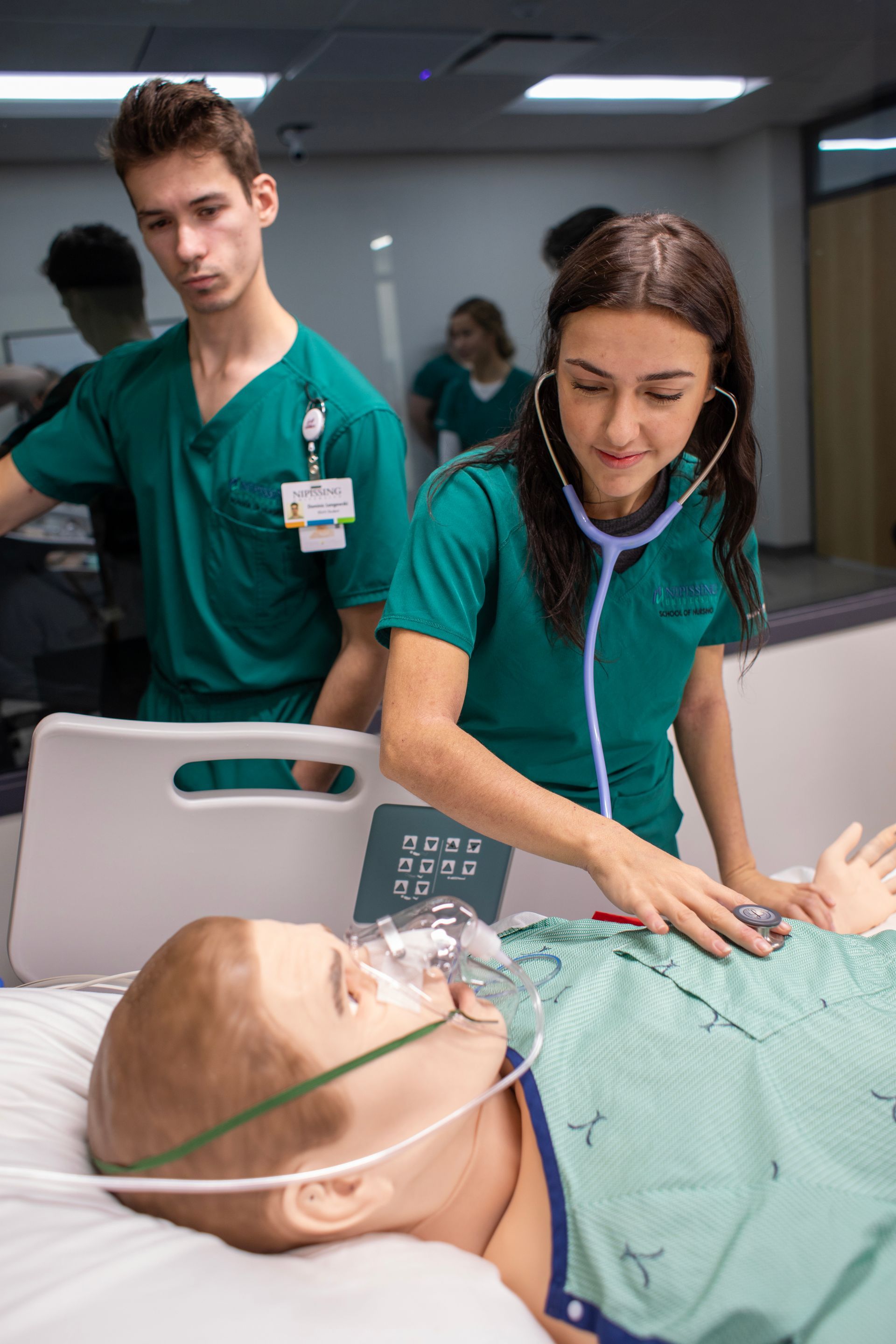 A man and a woman are examining a mannequin in a hospital bed.
