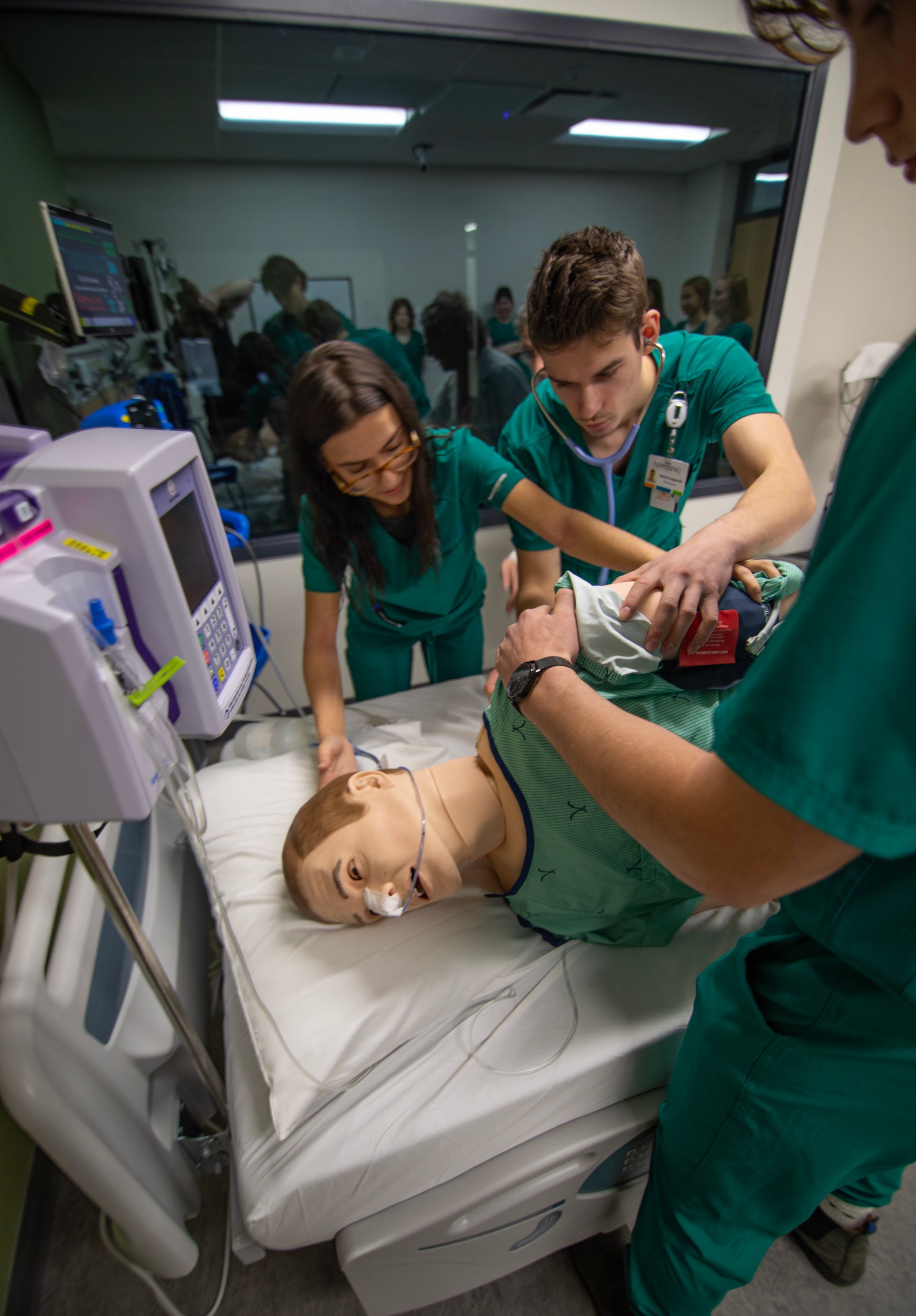 A group of nurses are working on a mannequin in a hospital room.