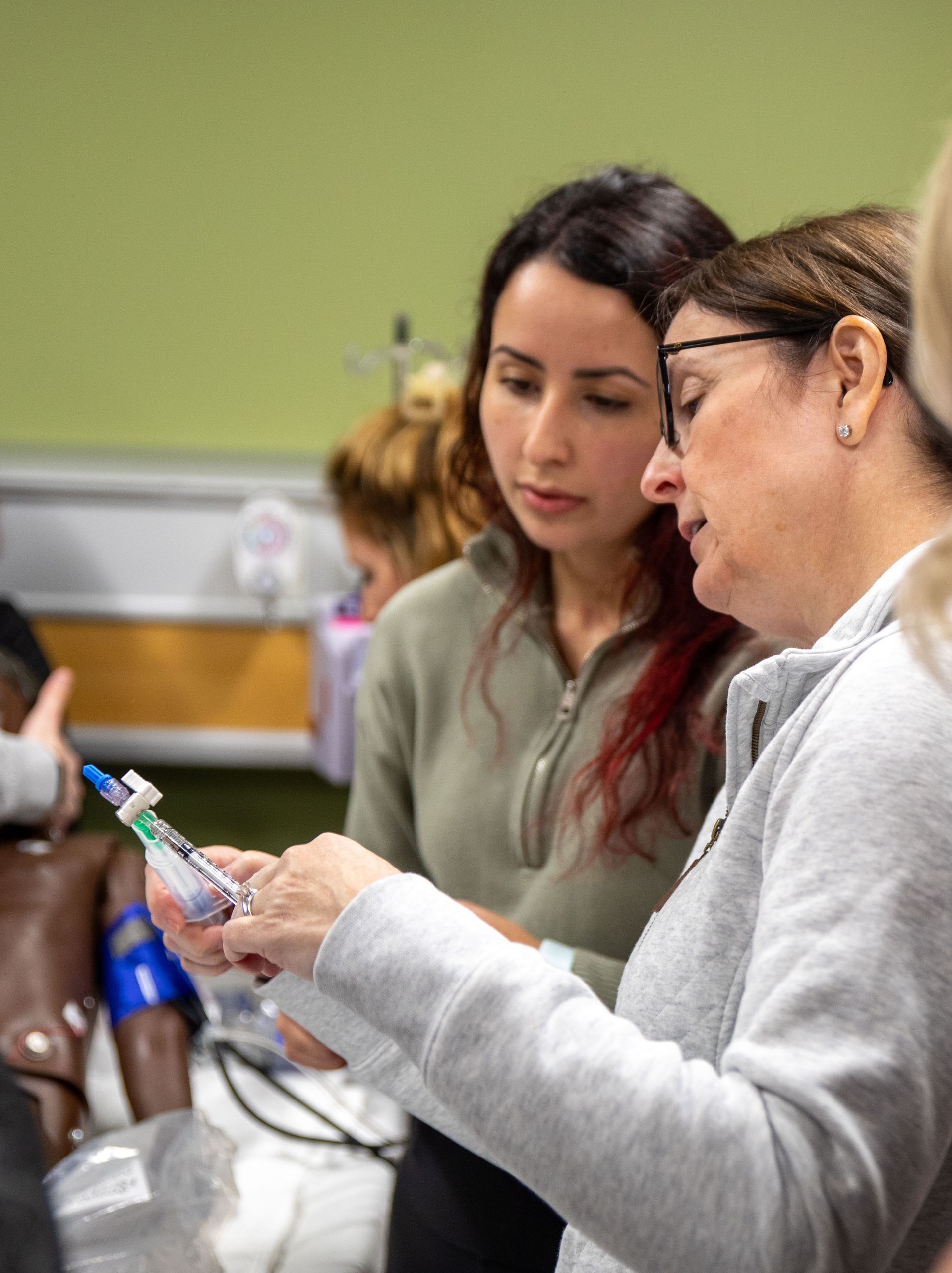 Two women are looking at a syringe in a hospital room.
