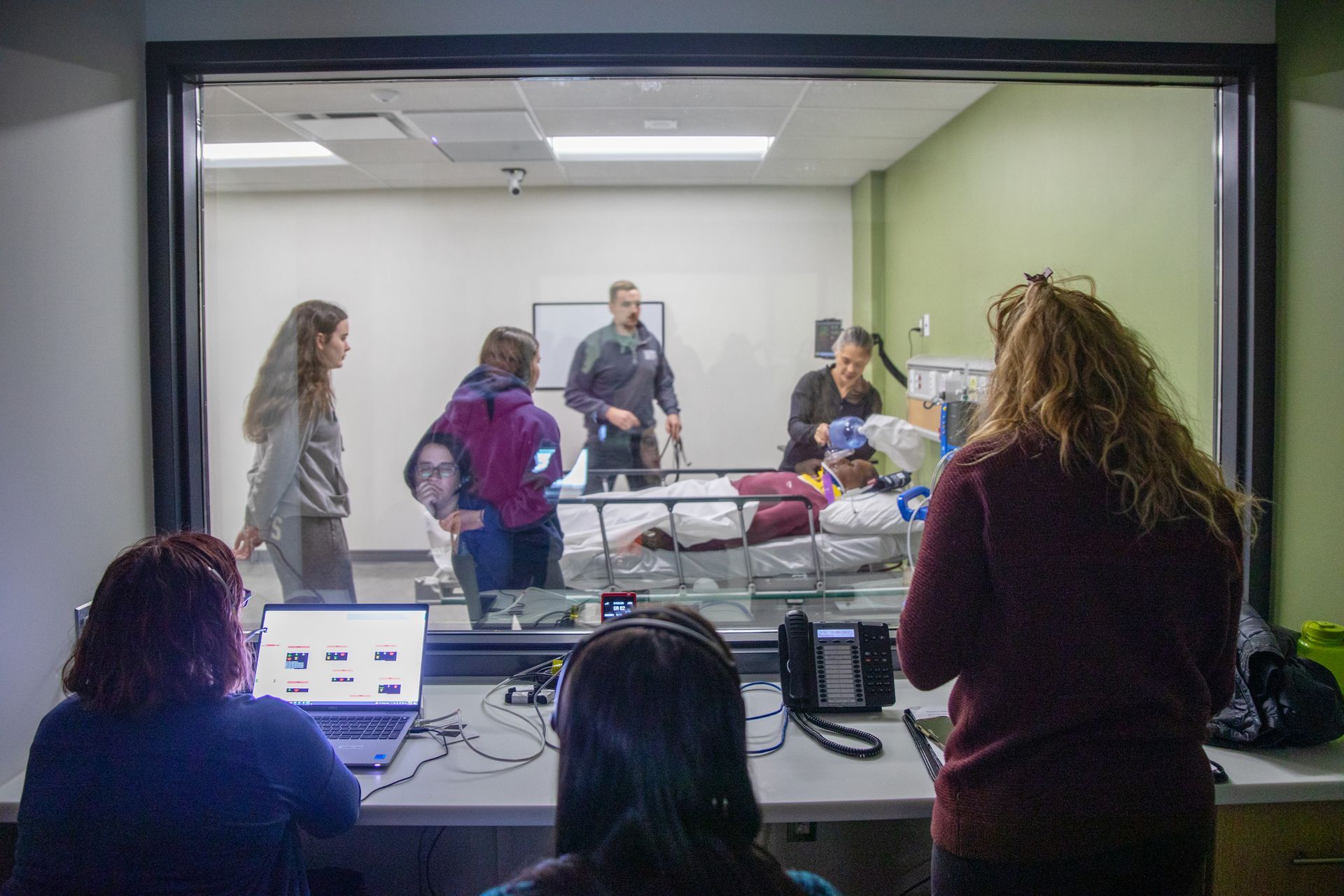 A group of people are looking at a patient in a hospital bed through a window.