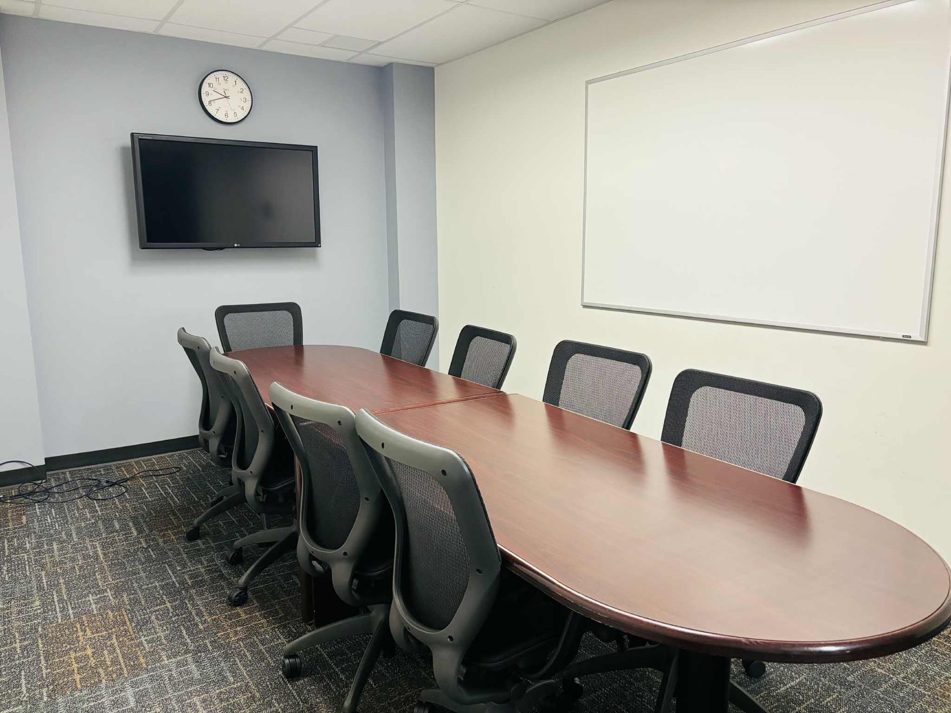 Conference room with a long oval table, chairs, a TV, and a whiteboard.