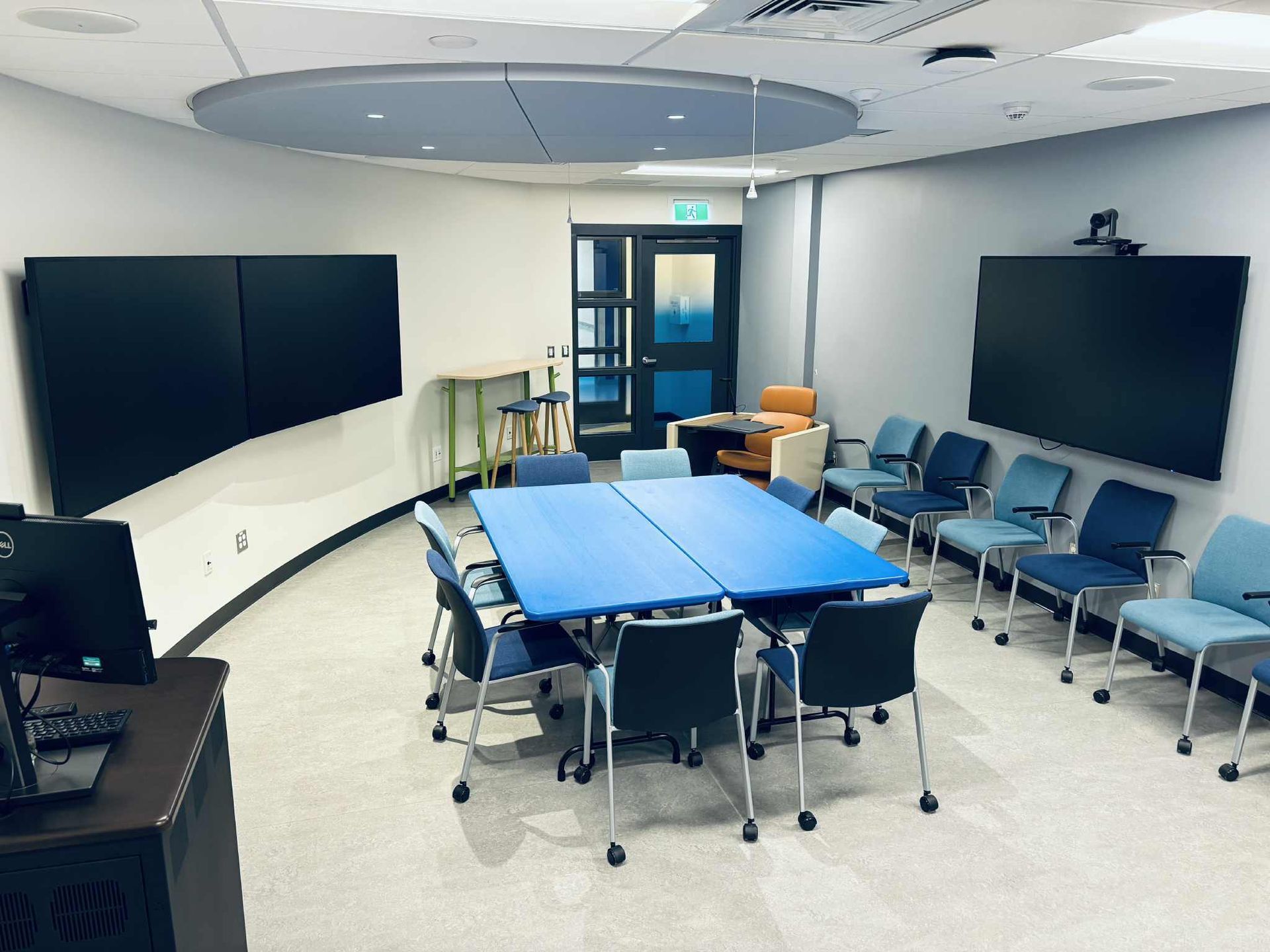 Conference room with blue table and chairs, large screens, and seating for a group.