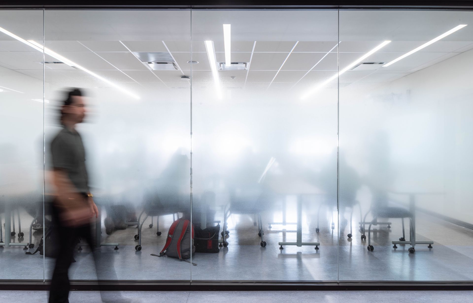 A blurry picture of a man walking in a room with a glass wall.