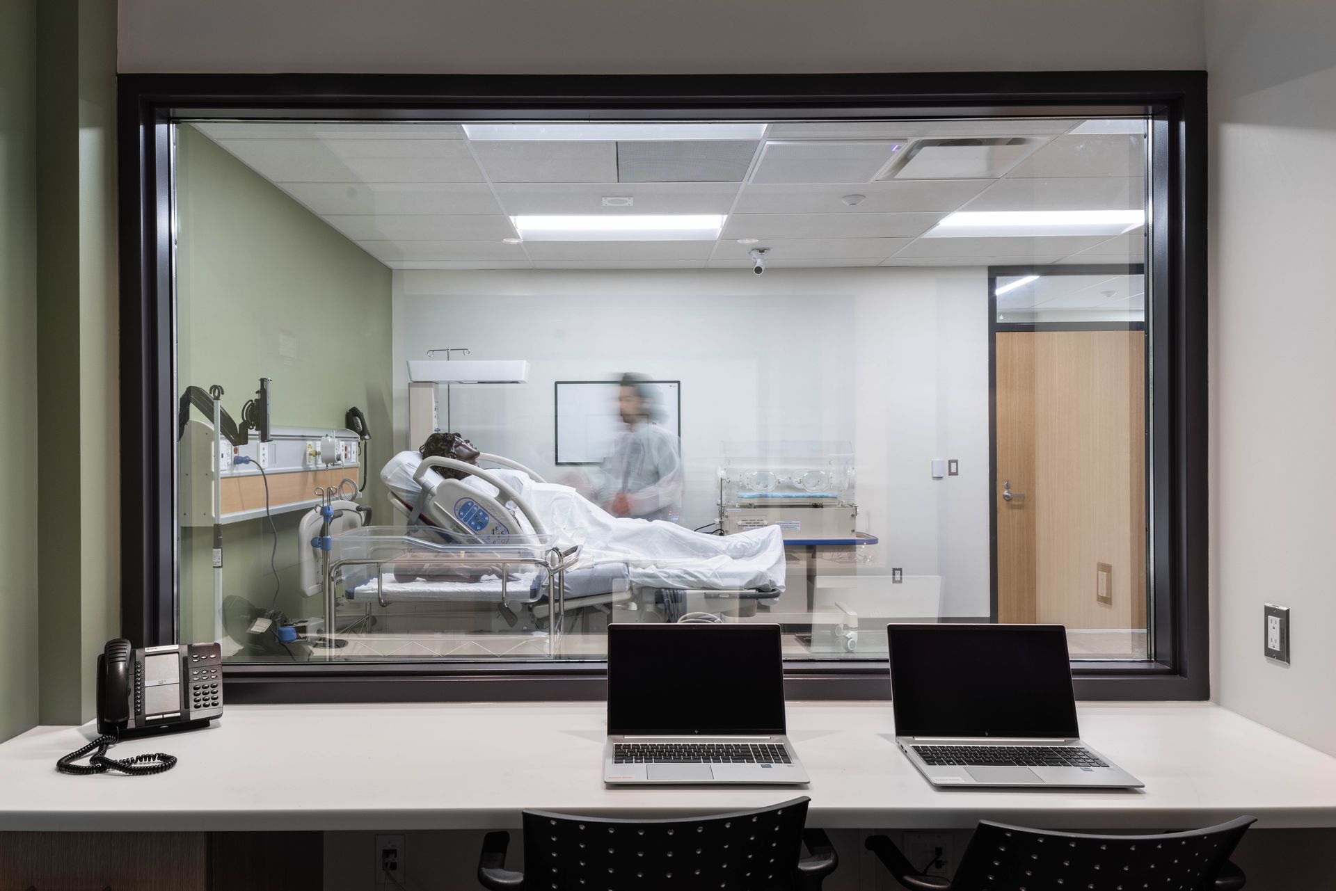 A hospital room with a view of a patient in a hospital bed through a window.