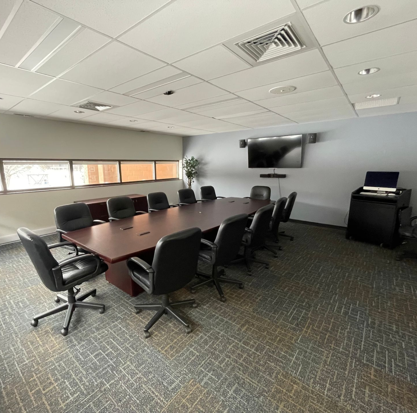 Conference room with long table, black chairs, TV, and a computer stand.