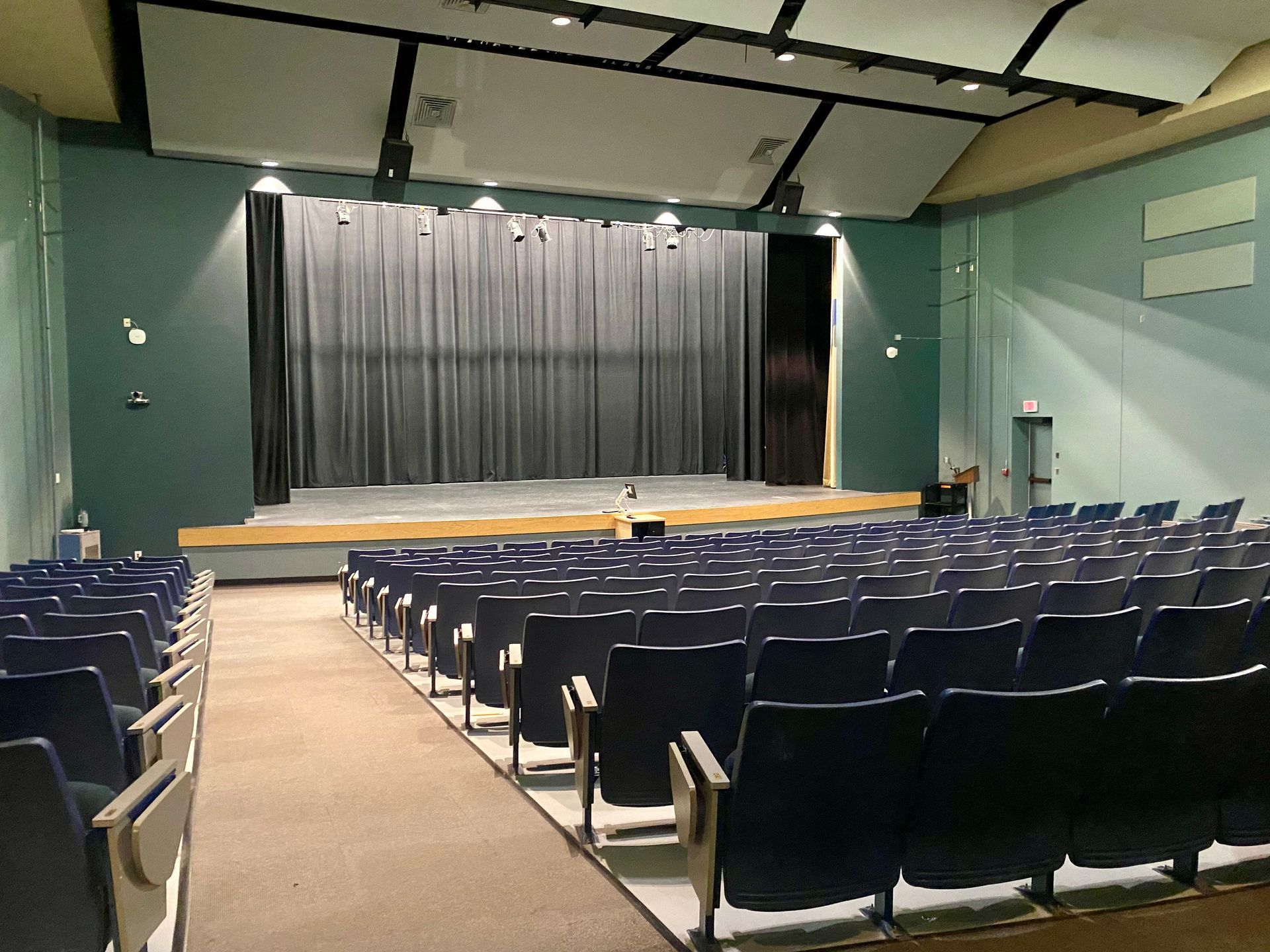 A modern classroom with green chairs, bean bags, large screens, and glass doors.