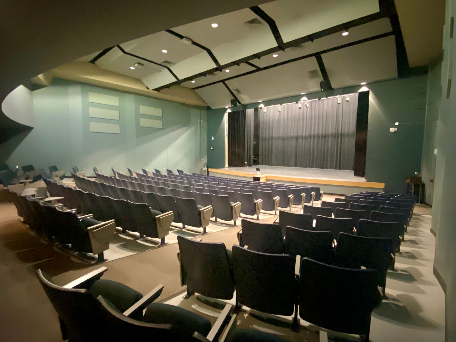 Rows of blue chairs face two large black screens in a modern classroom setting.