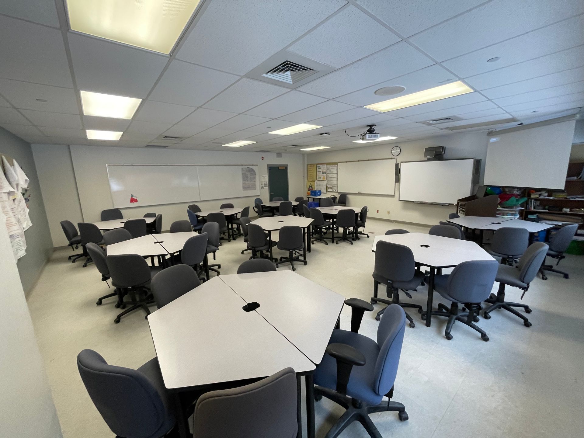 Classroom with hexagonal tables, chairs, whiteboards, and ceiling lights.
