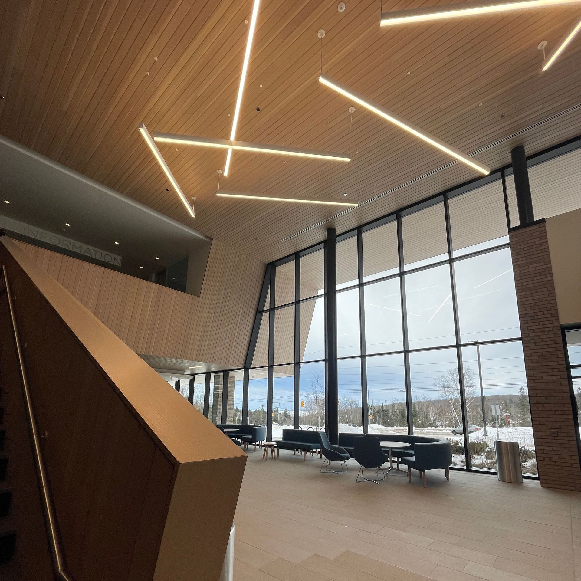 Interior view of a modern building with a wood ceiling, large windows, and seating area.