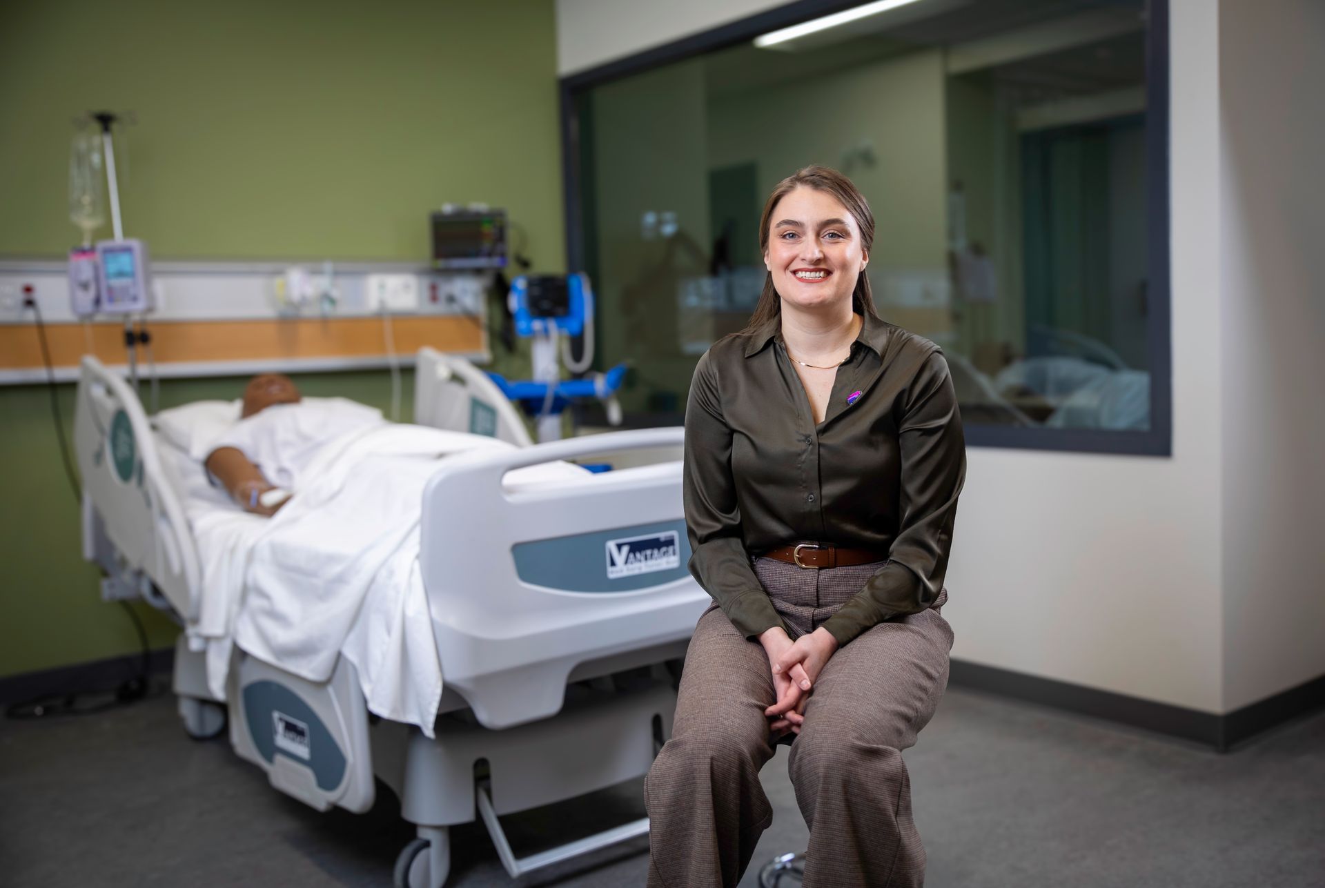 A woman is sitting in a hospital room next to a hospital bed.