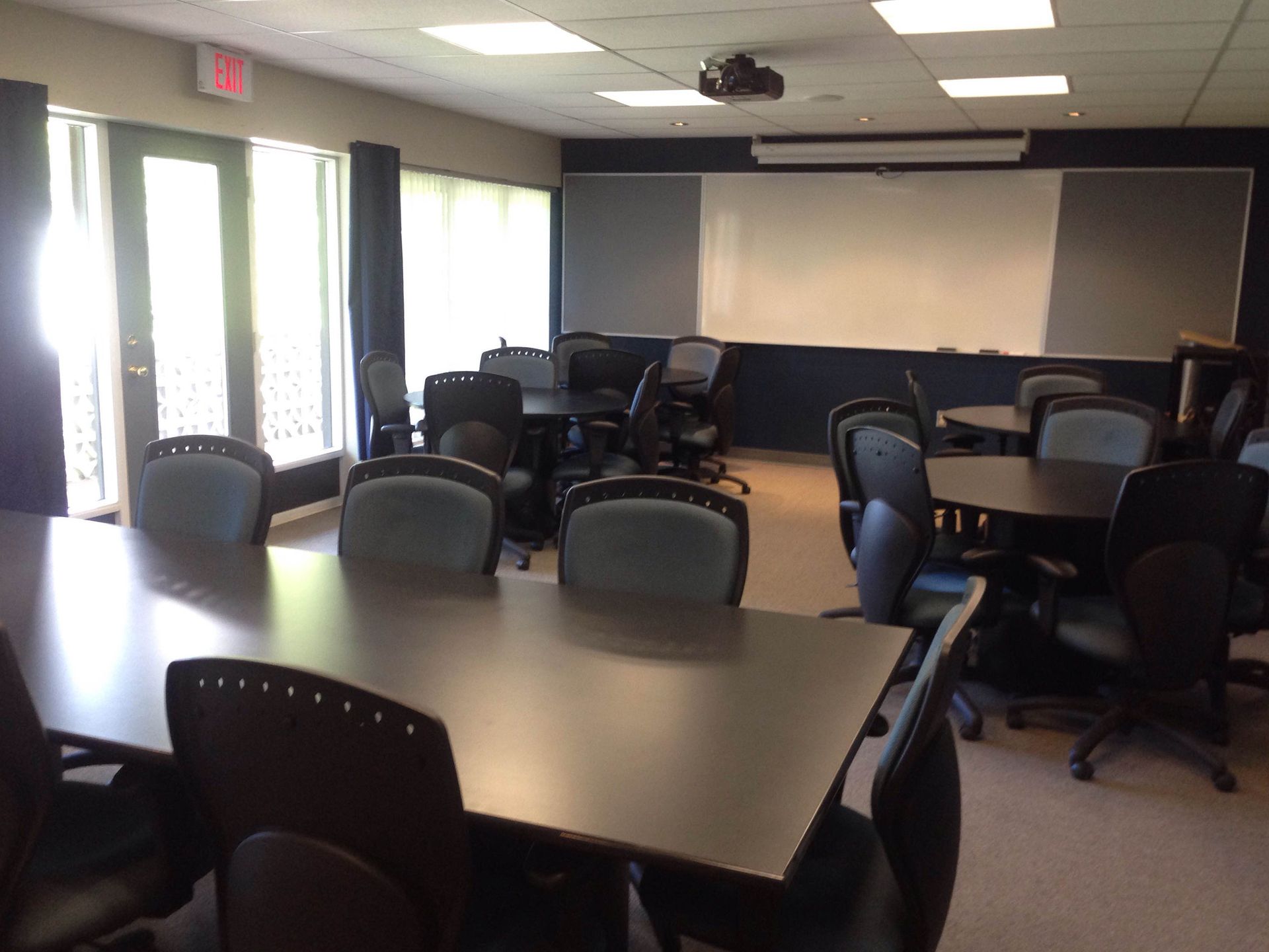 Classroom with tables, chairs, whiteboard, projector, and windows with curtains.