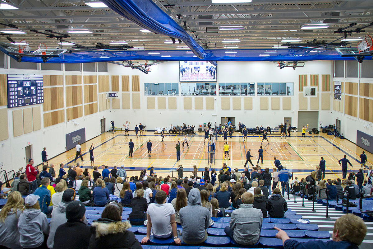 A crowd of people are watching a volleyball game in a gym.