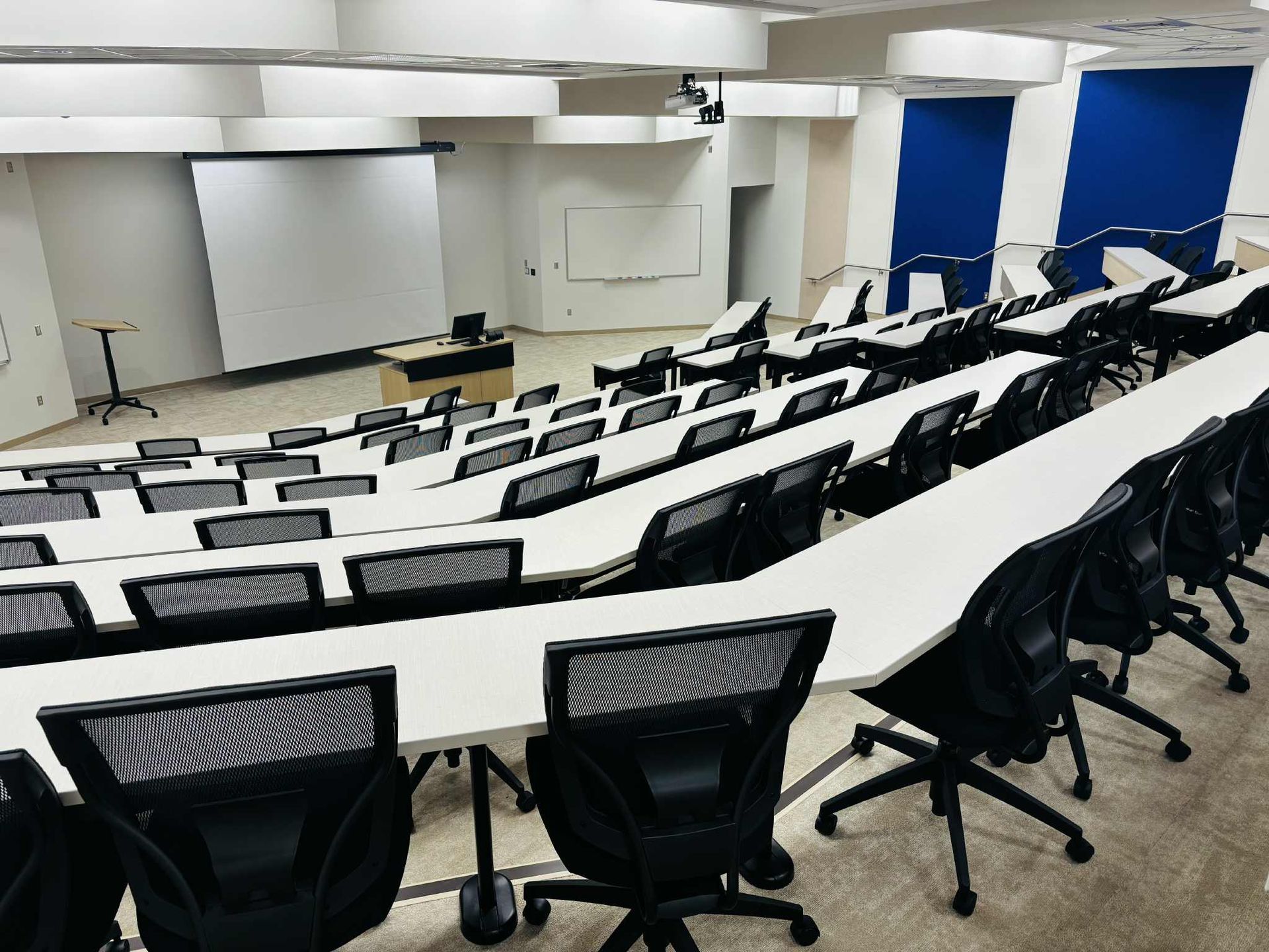 Large lecture hall with students taking notes as a professor lectures.