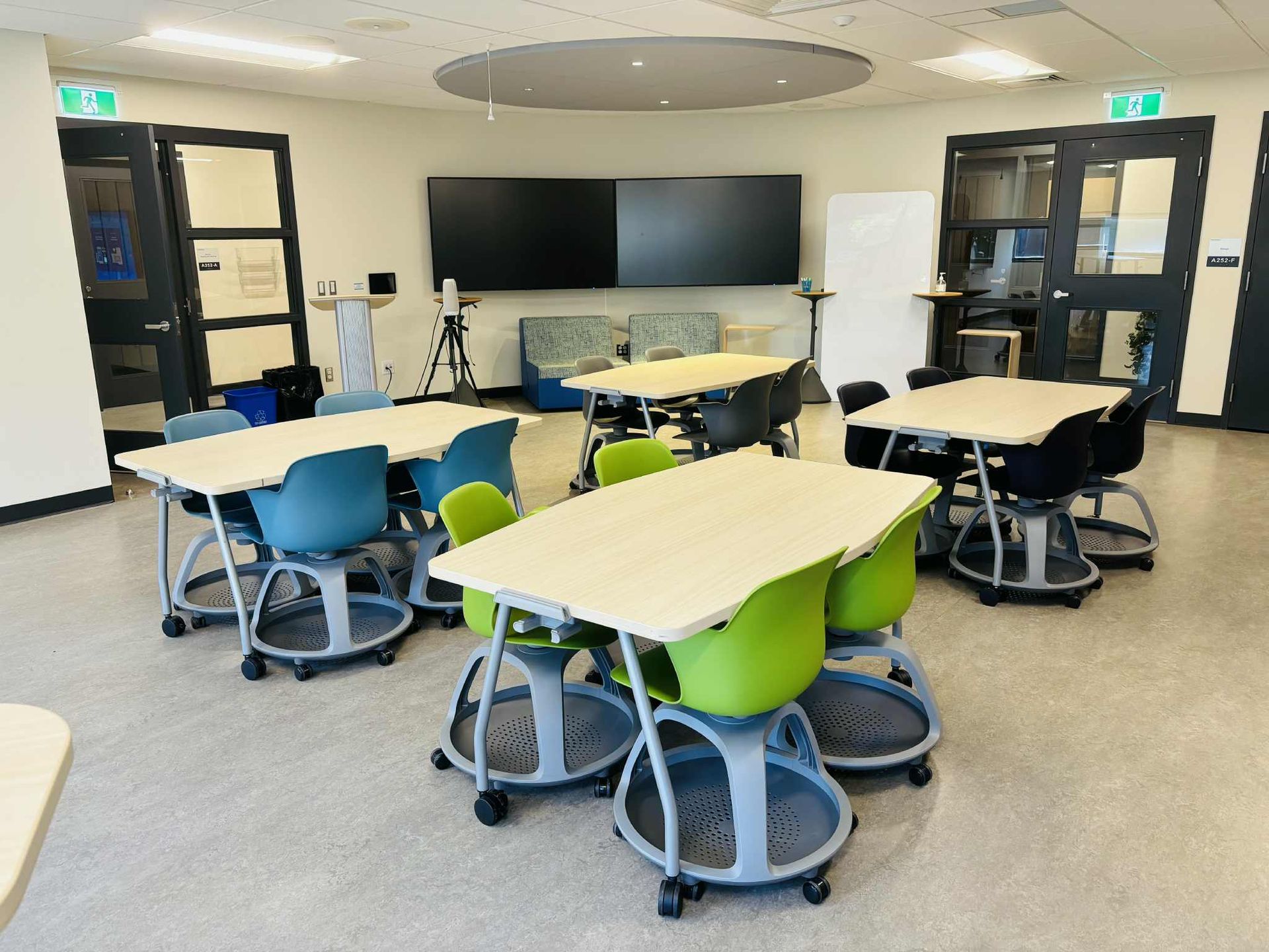 Bright classroom with bean bags, a white board, large screens, tables, and chairs.