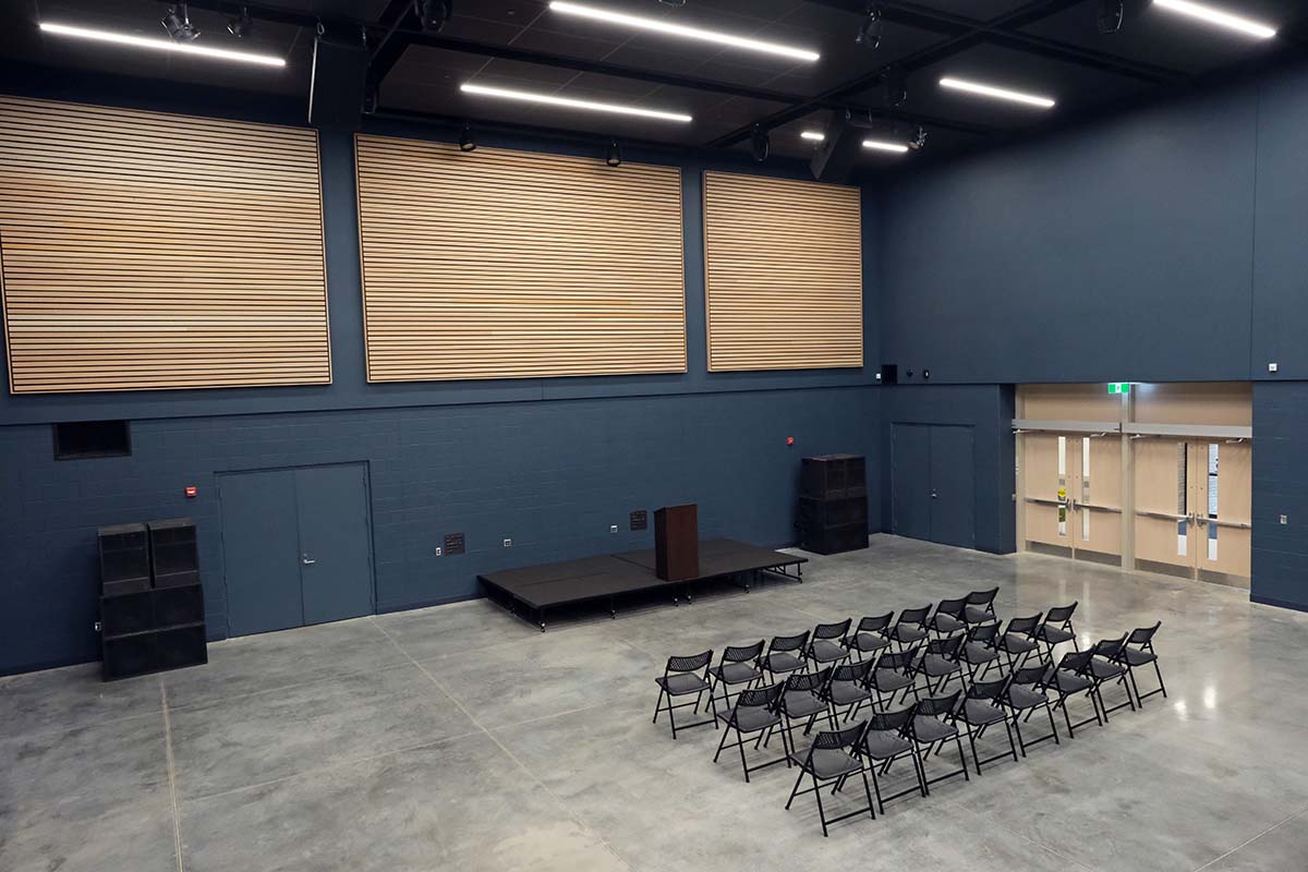 A large, modern event space with wood paneling, stage, seating, speakers, and blue walls.