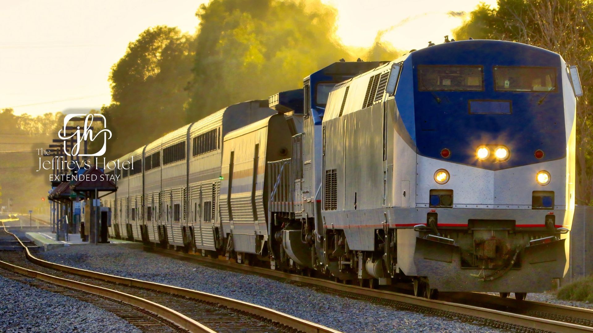 An Amtrak train in Osceola, Iowa with blue and silver cars travels on tracks in the sunlight.