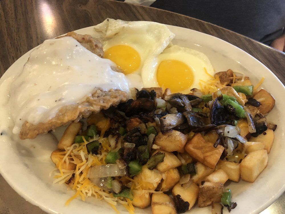 Plate of breakfast food with fried potatoes, eggs, gravy-covered meat, and cheese.