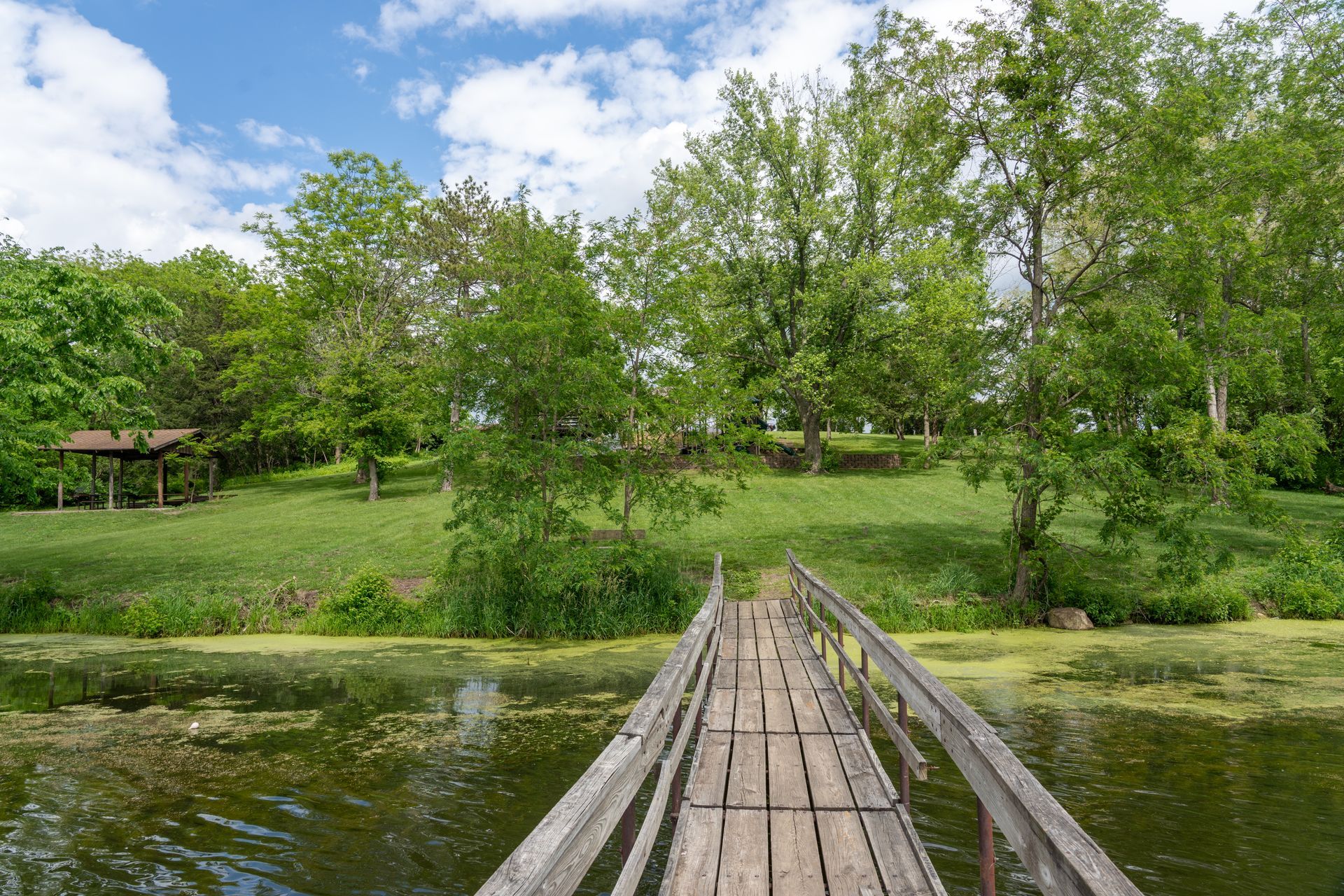 Wooden fishing dock leading to grassy hill surrounded by trees at East Lake Park in Osceola, Iowa