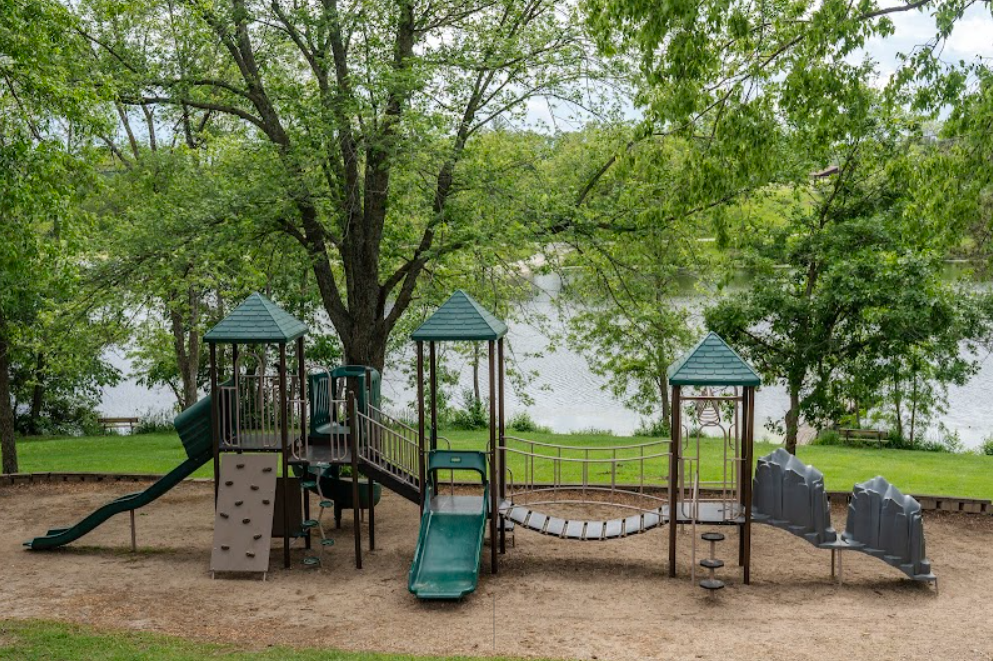 Children's playground set by the lake with slides and climbing areas under shade trees at East Lake Park in Osceola, Iowa