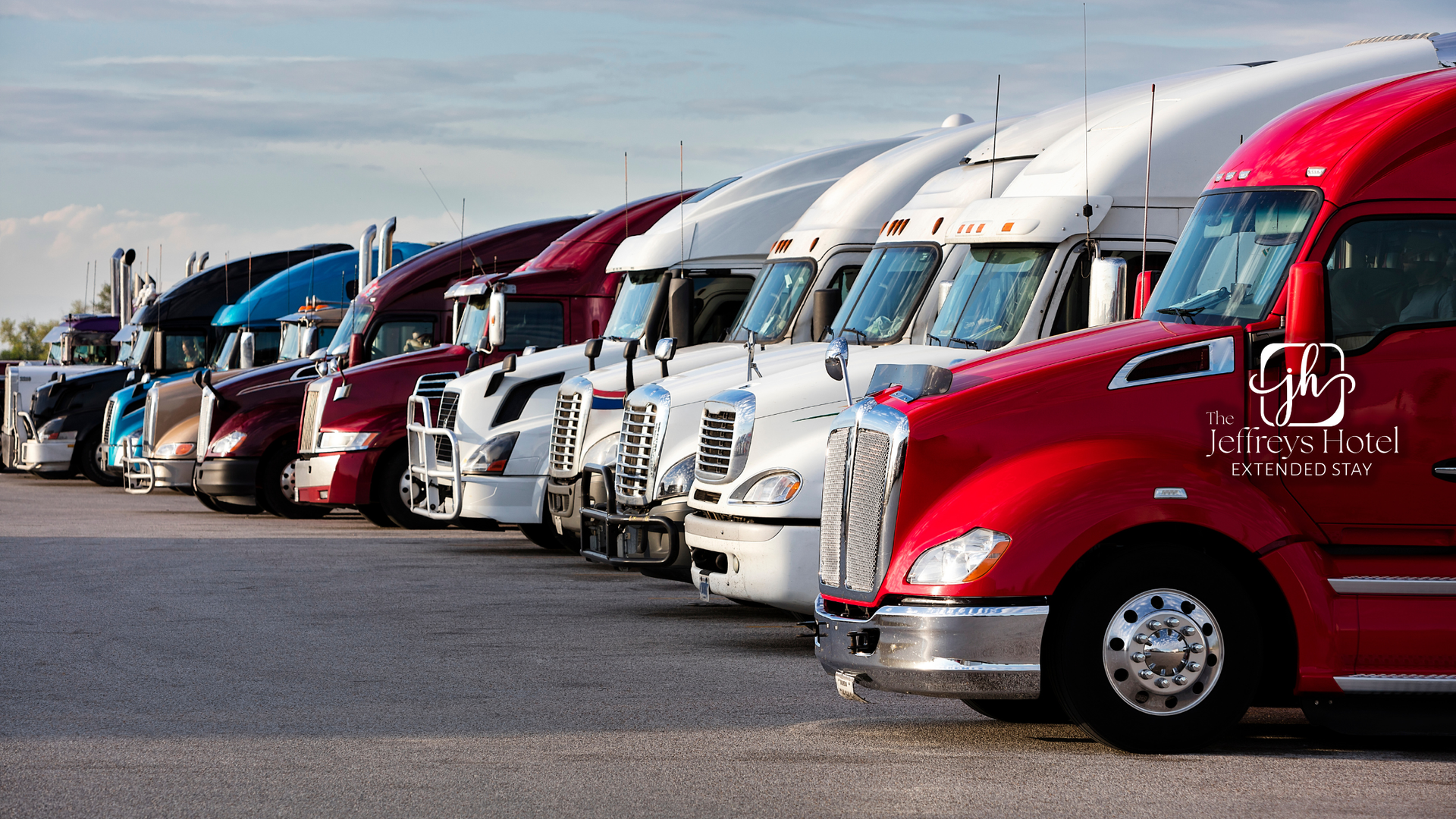 Row of semi-trucks parked at a truck stop, varying colors including red, white, blue, and black.