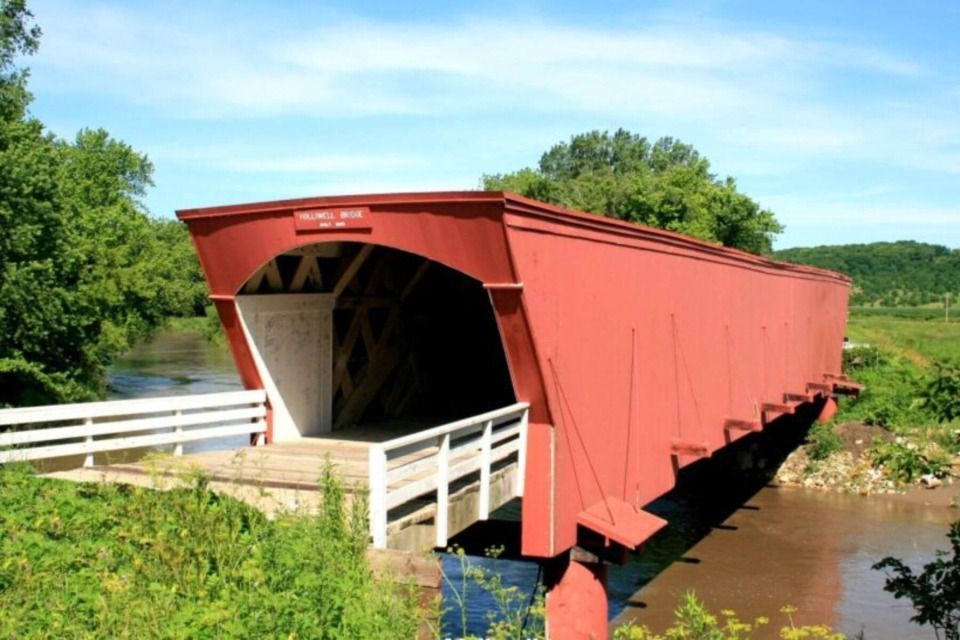 Red covered bridge over a river, white railings, green foliage, sunny day, Madison County, Iowa