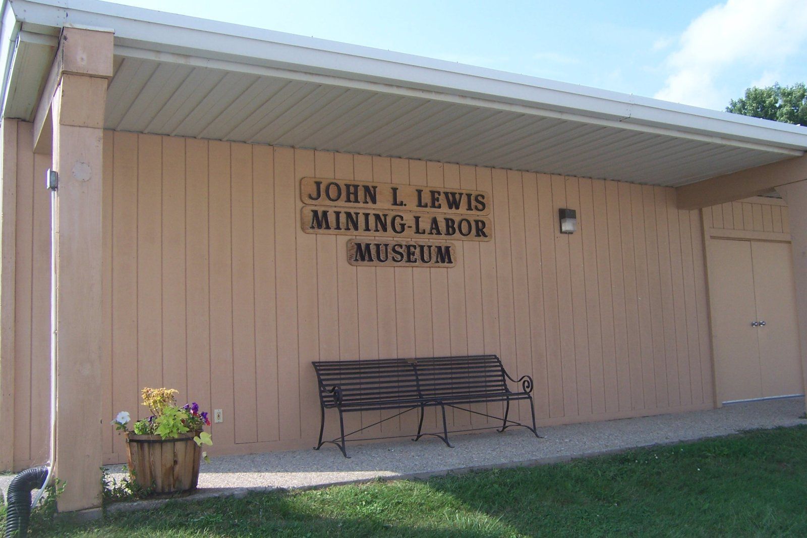 John L. Lewis Mining-Labor Museum building with brown facade, sign, bench, and flower pot.